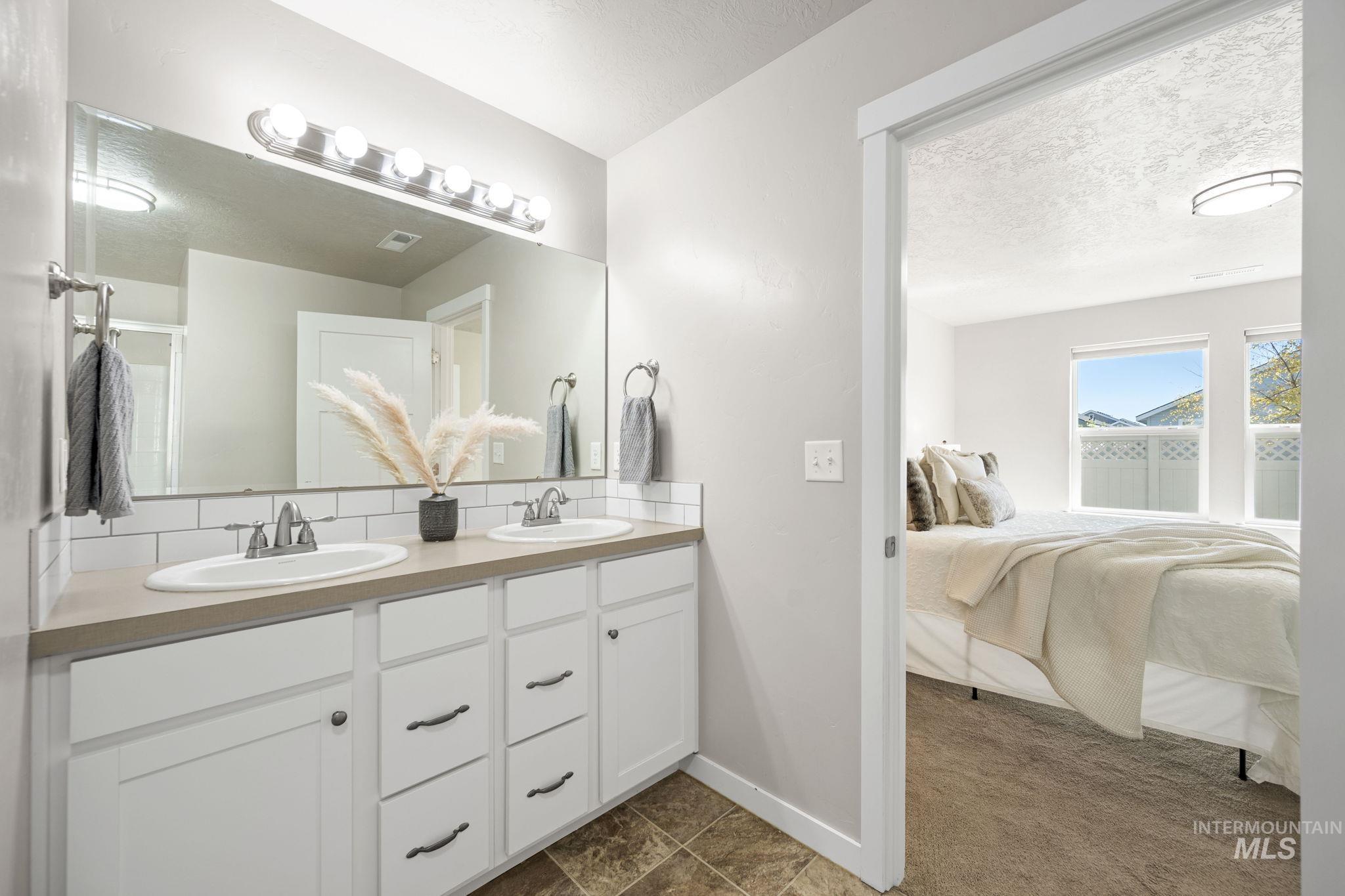 Ensuite bathroom featuring double vanity, a textured ceiling, and backsplash