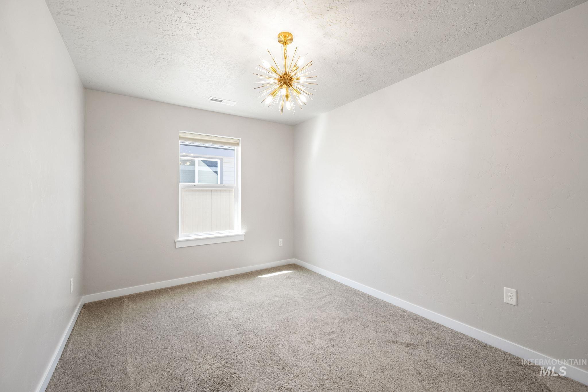 Spare room featuring light carpet, a textured ceiling, and a chandelier