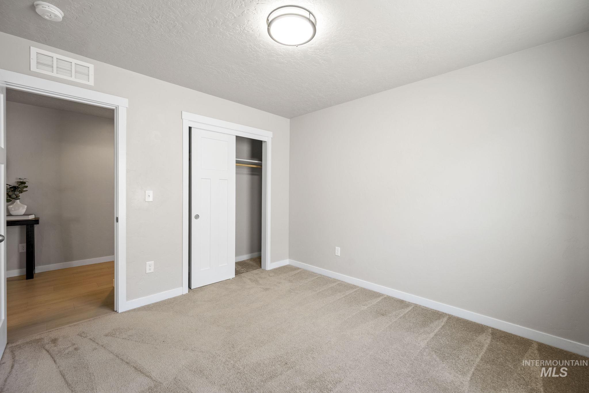Unfurnished bedroom featuring a textured ceiling, a closet, and light colored carpet