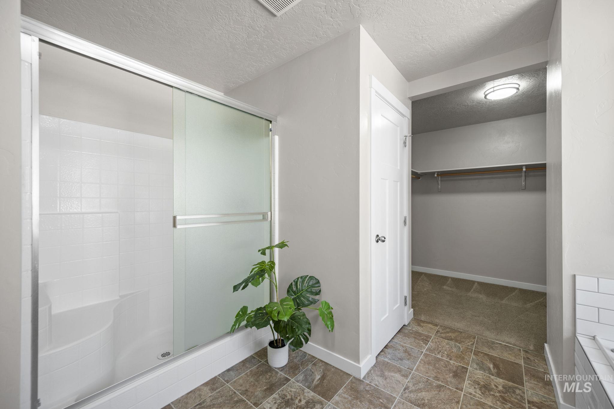 Bathroom featuring a textured ceiling, a stall shower, a spacious closet, and stone finish flooring