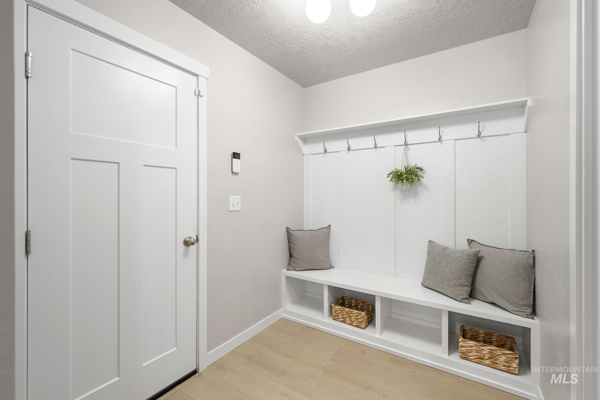 Mudroom with light wood-style flooring, built in bench, coat rack and a textured ceiling