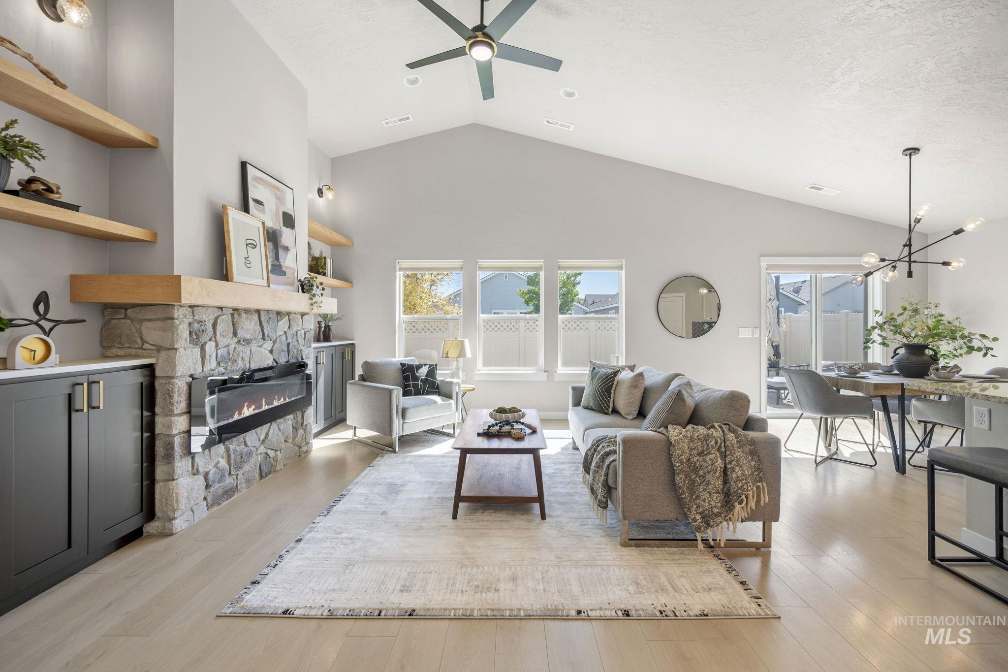 Living area featuring light wood-style flooring, high vaulted ceiling, a fireplace, a chandelier, and a ceiling fan