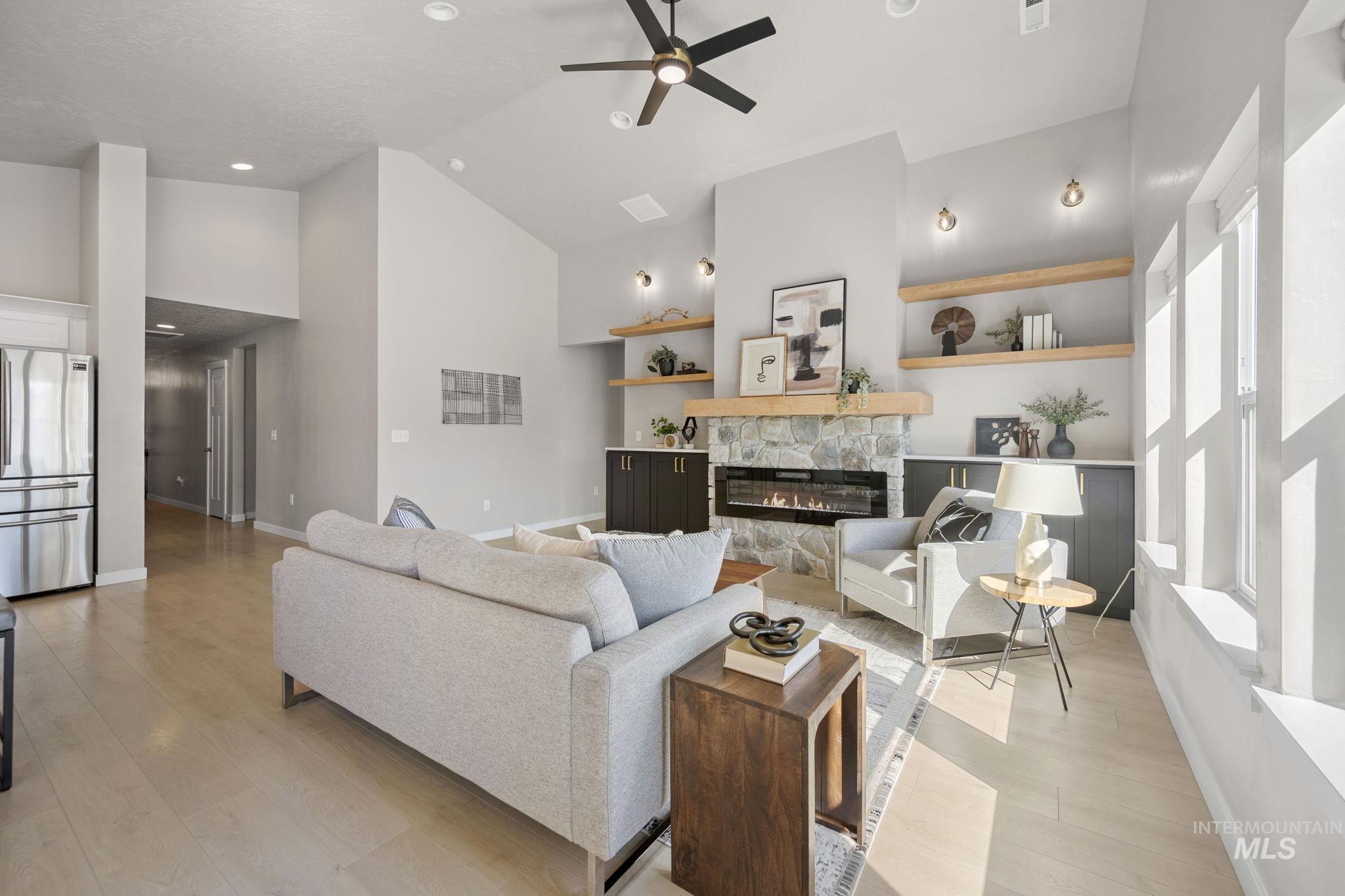 Living room featuring light wood-type flooring, a stone fireplace, high vaulted ceiling, a ceiling fan, and recessed lighting