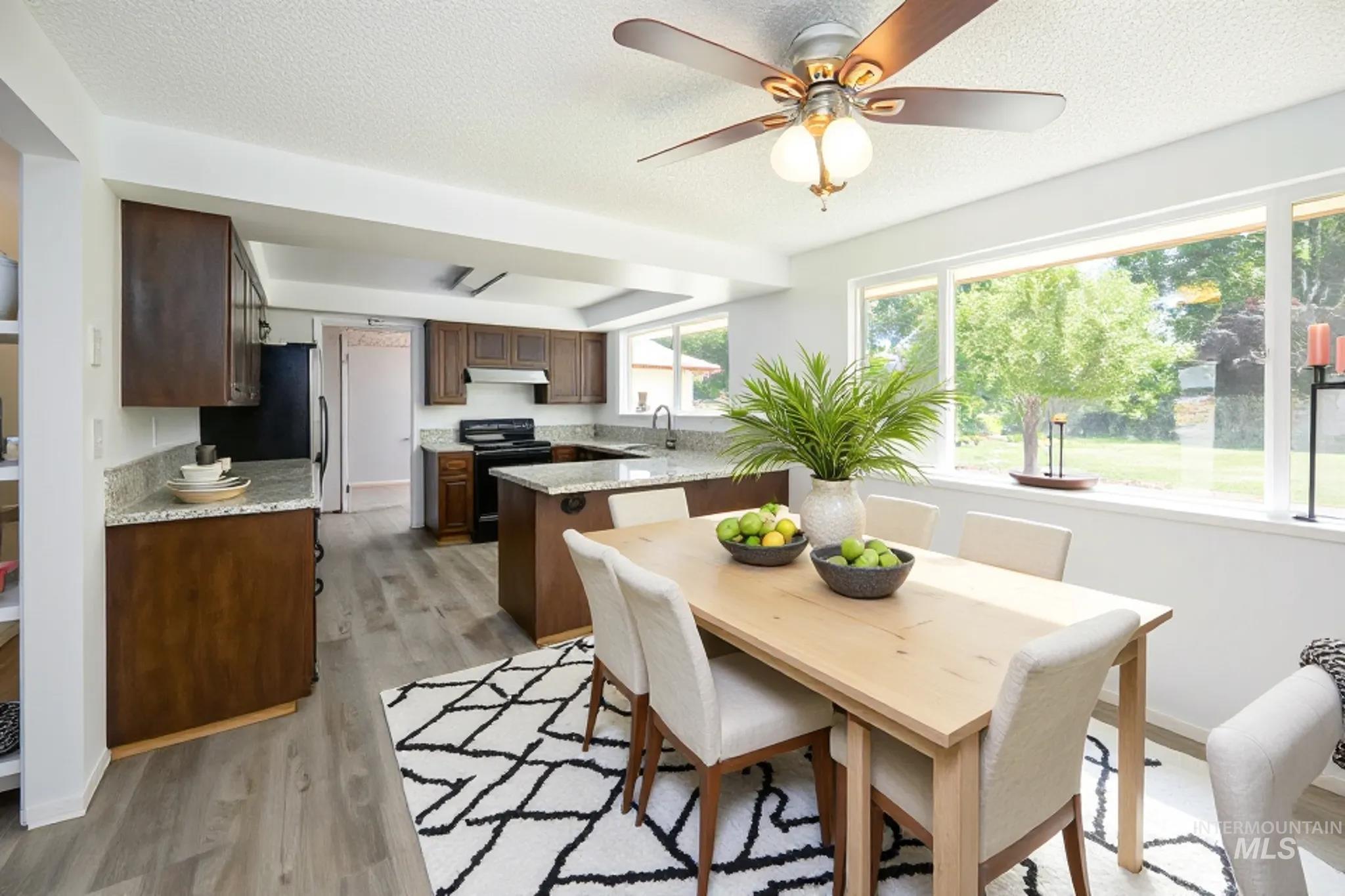 Kitchen with light wood-type flooring, a peninsula, light stone countertops, black / electric stove, and a textured ceiling