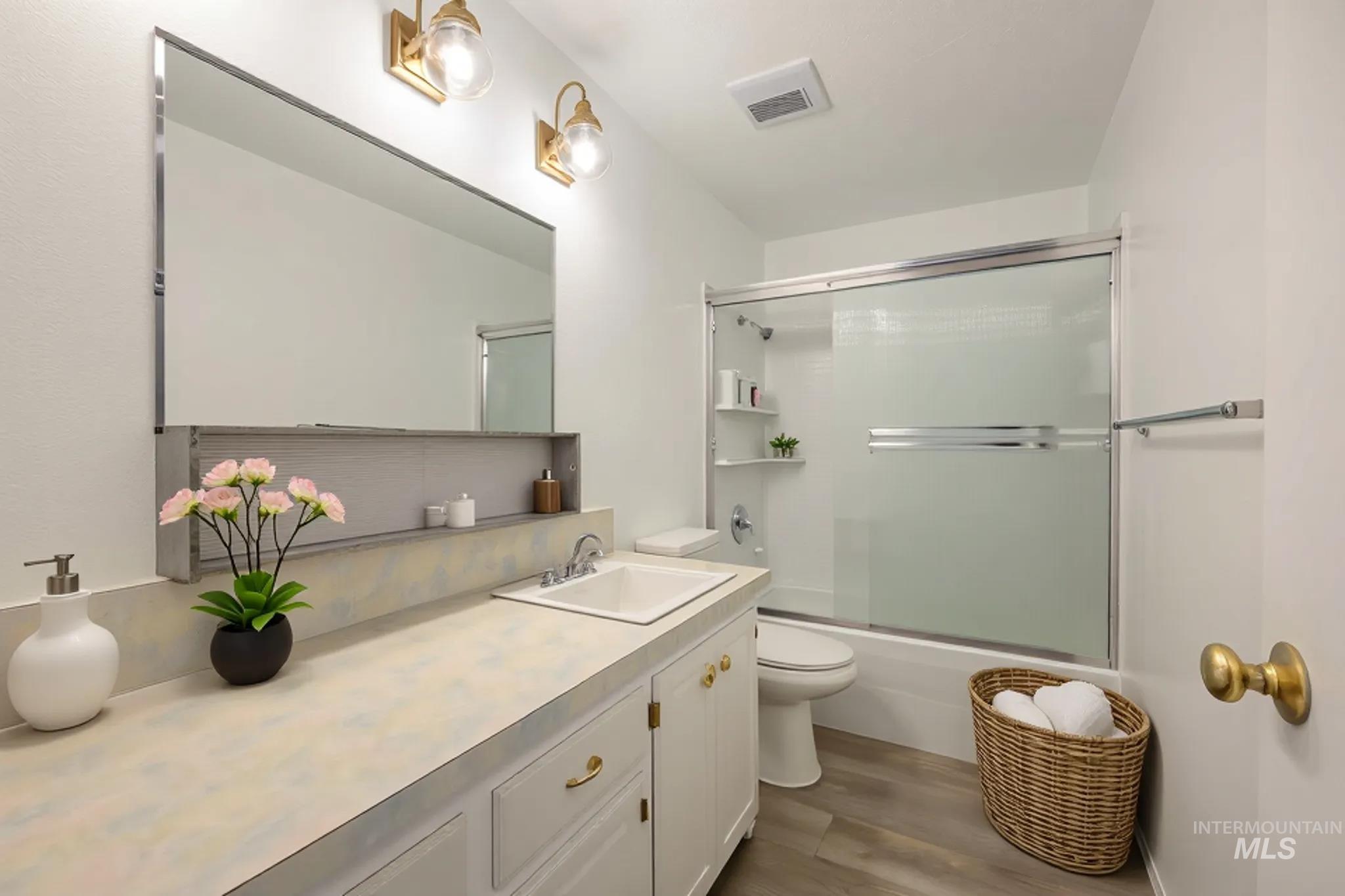Full bath with combined bath / shower with glass door, dark wood-style floors, and vanity