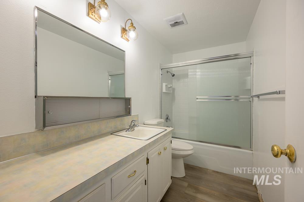 Bathroom with combined bath / shower with glass door, dark wood finished floors, and vanity