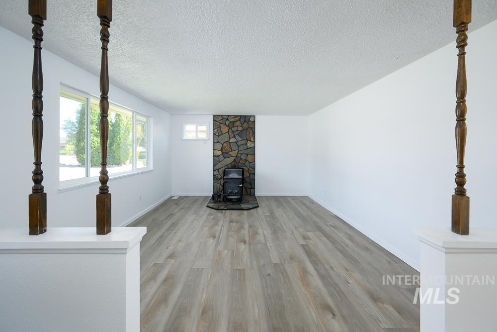 Unfurnished living room featuring a wood stove, light wood-style floors, and a textured ceiling