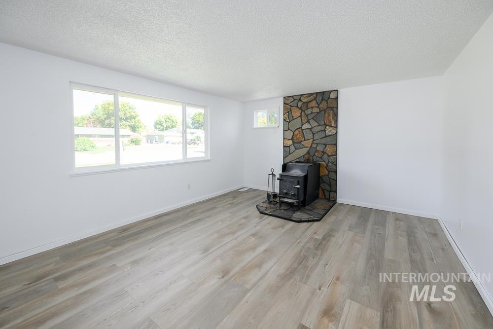 Unfurnished living room with a wood stove, a textured ceiling, and light wood-style flooring
