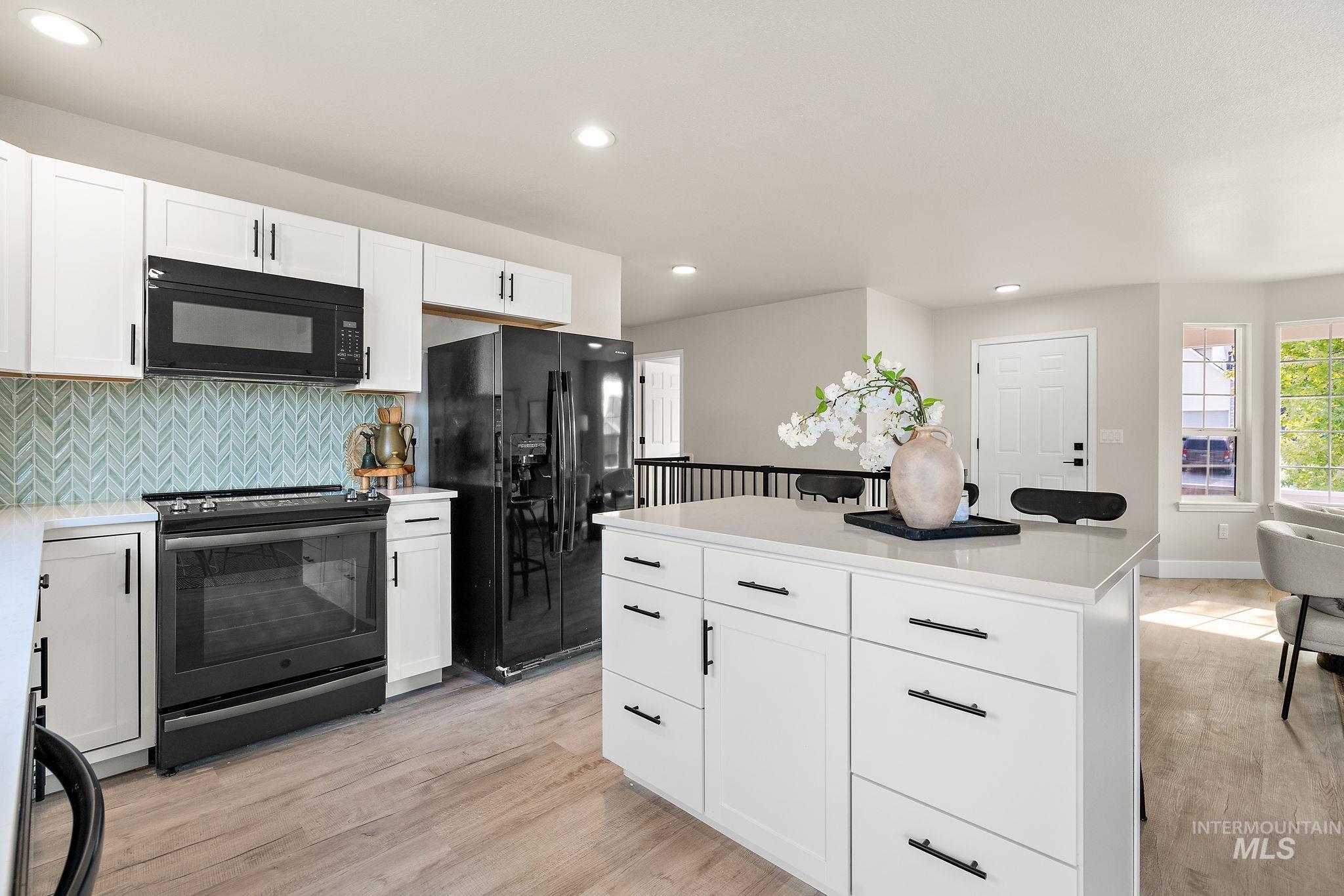 Kitchen featuring white cabinets, black appliances, tasteful backsplash, recessed lighting, and light wood-style floors