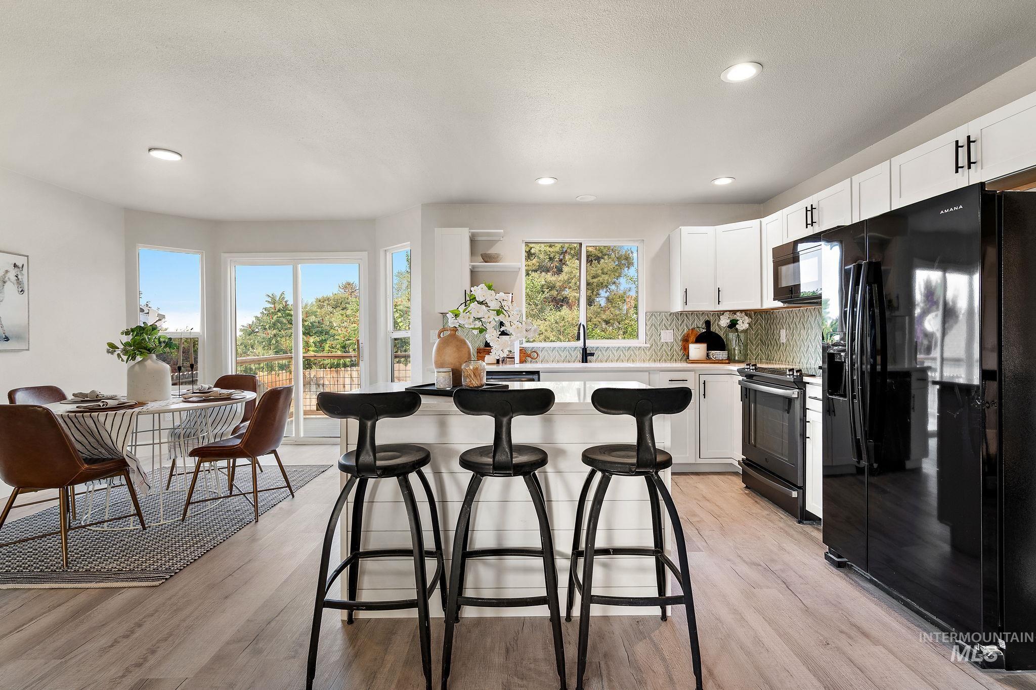 Kitchen featuring black appliances, white cabinets, decorative backsplash, light countertops, and light wood-style flooring