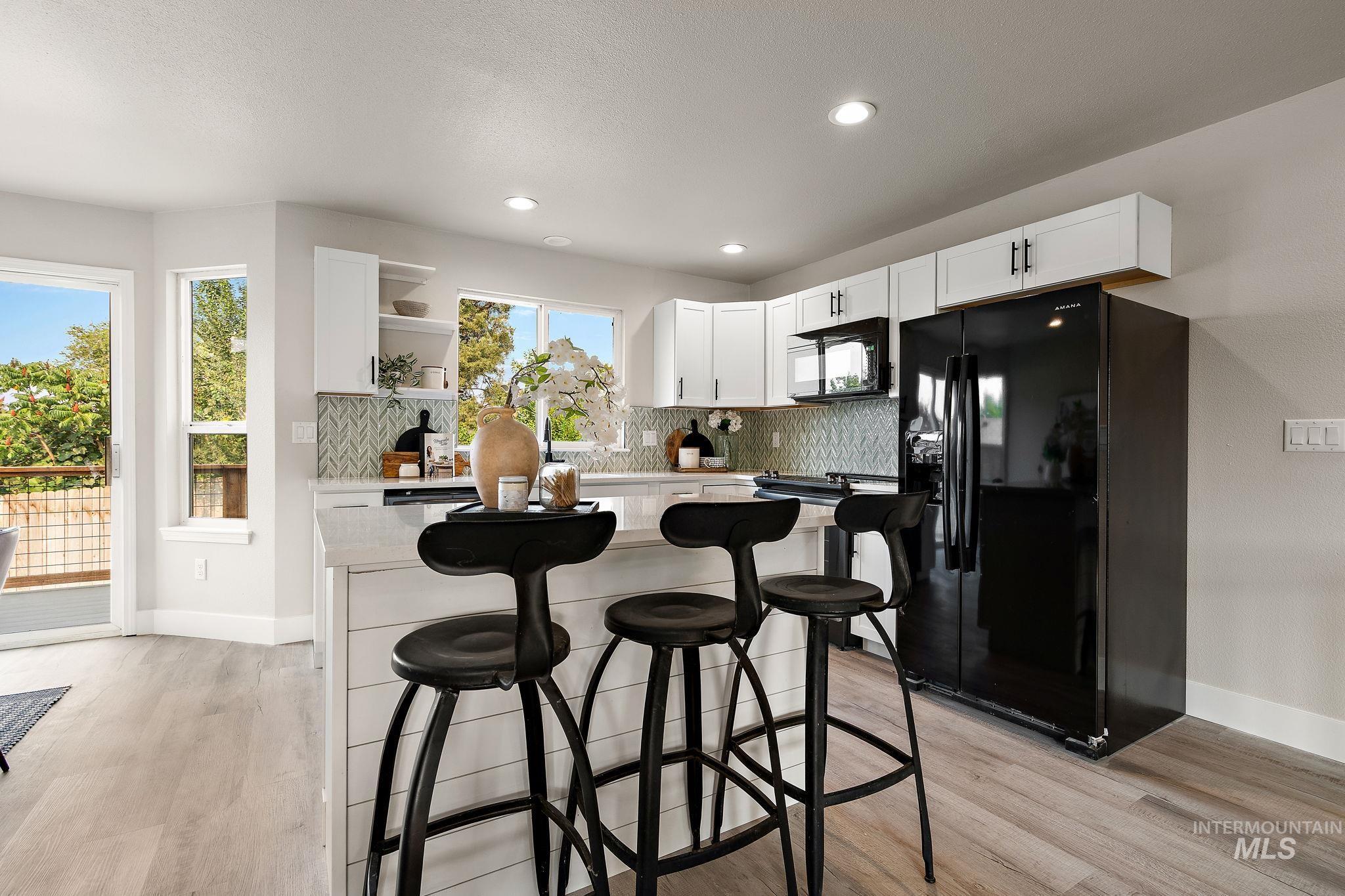 Kitchen featuring black appliances, tasteful backsplash, a breakfast bar, white cabinets, and open shelves