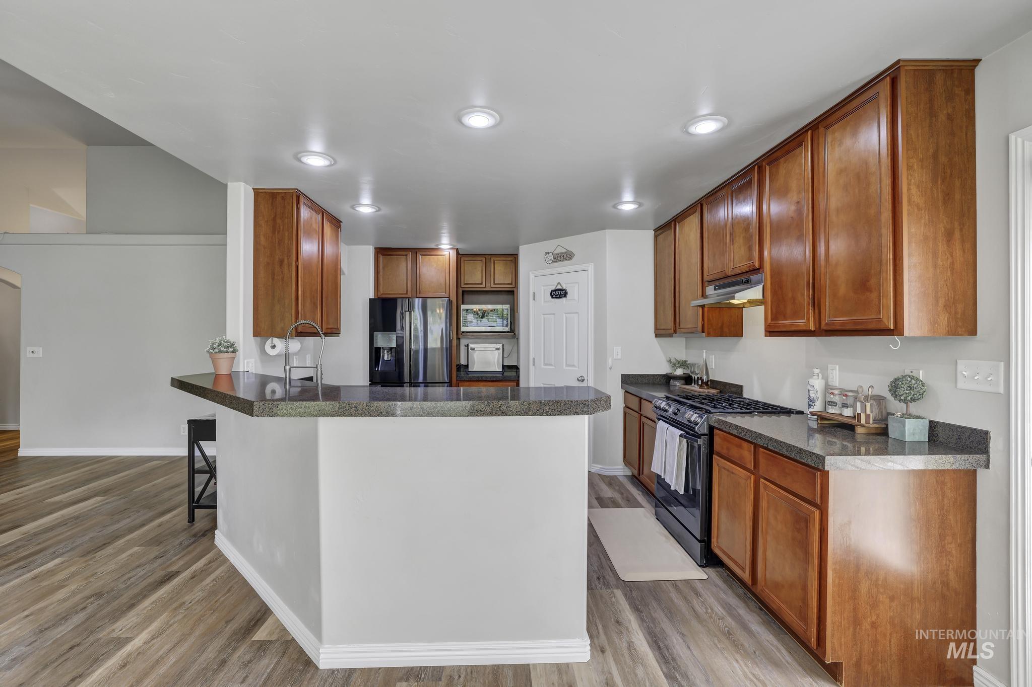Kitchen featuring dark countertops, black gas range oven, brown cabinets, refrigerator with ice dispenser, and recessed lighting