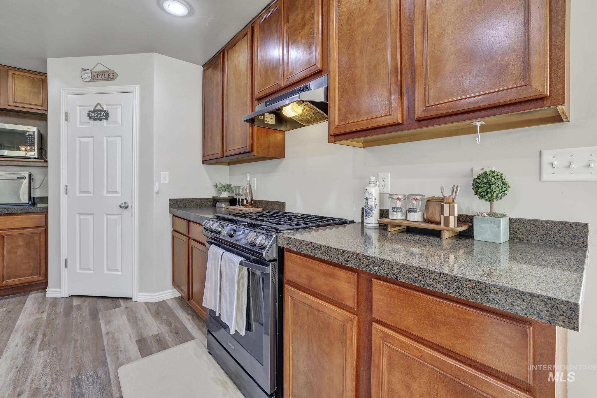 Kitchen featuring appliances with stainless steel finishes, brown cabinetry, under cabinet range hood, light wood-type flooring, and recessed lighting