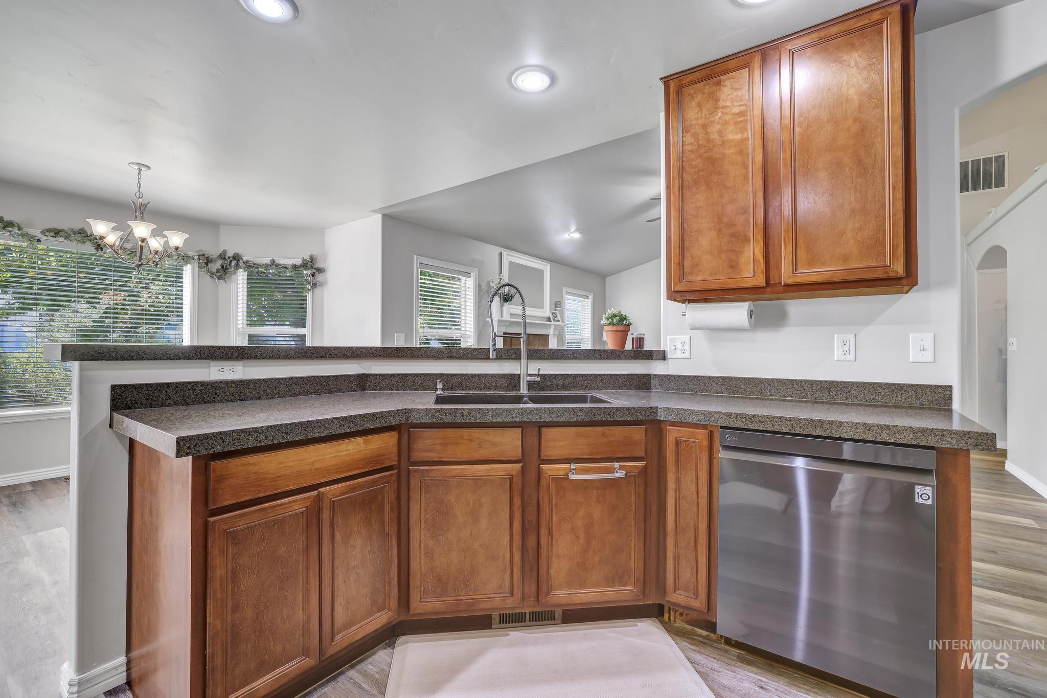 Kitchen featuring brown cabinetry, stainless steel dishwasher, light wood-style flooring, a chandelier, and a peninsula