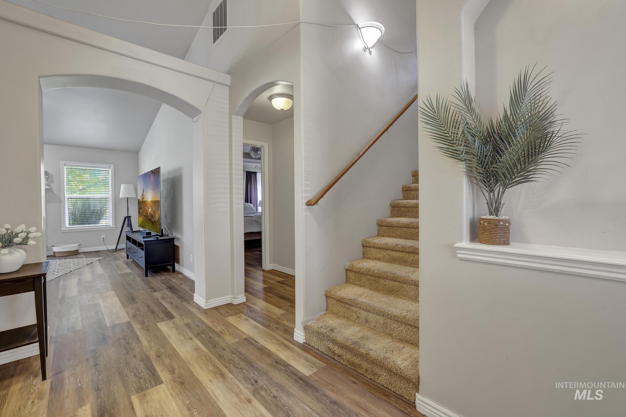Staircase with arched walkways, wood finished floors, and lofted ceiling