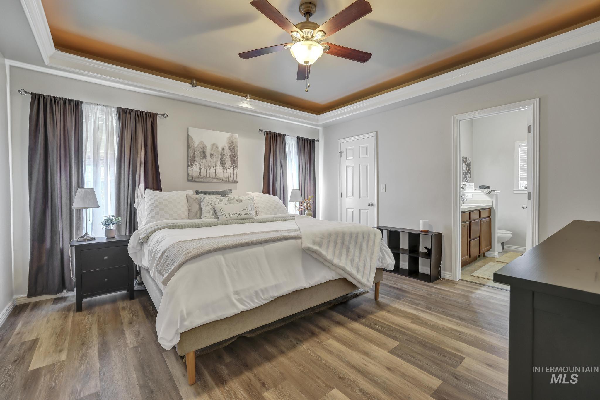 Bedroom featuring a raised ceiling, wood finished floors, connected bathroom, and a ceiling fan