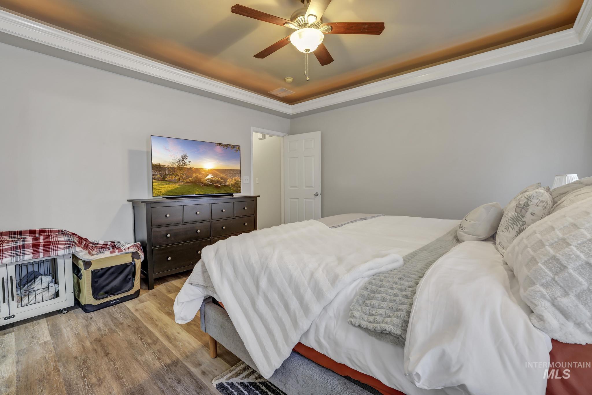 Bedroom with a tray ceiling, wood finished floors, ceiling fan, and ornamental molding