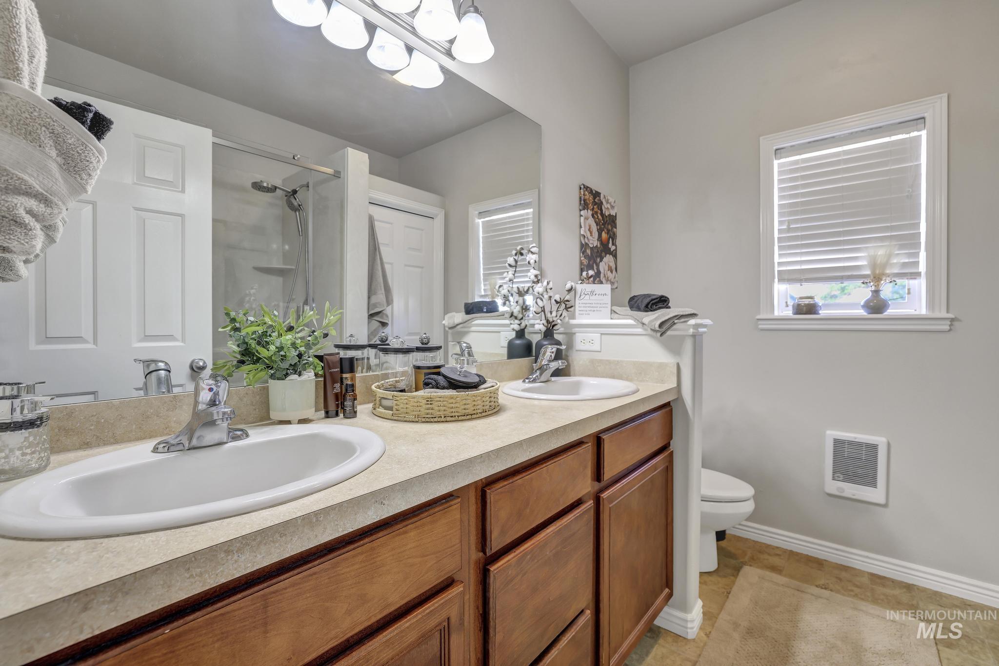 Full bath featuring double vanity, a shower, light tile patterned flooring, and heating unit