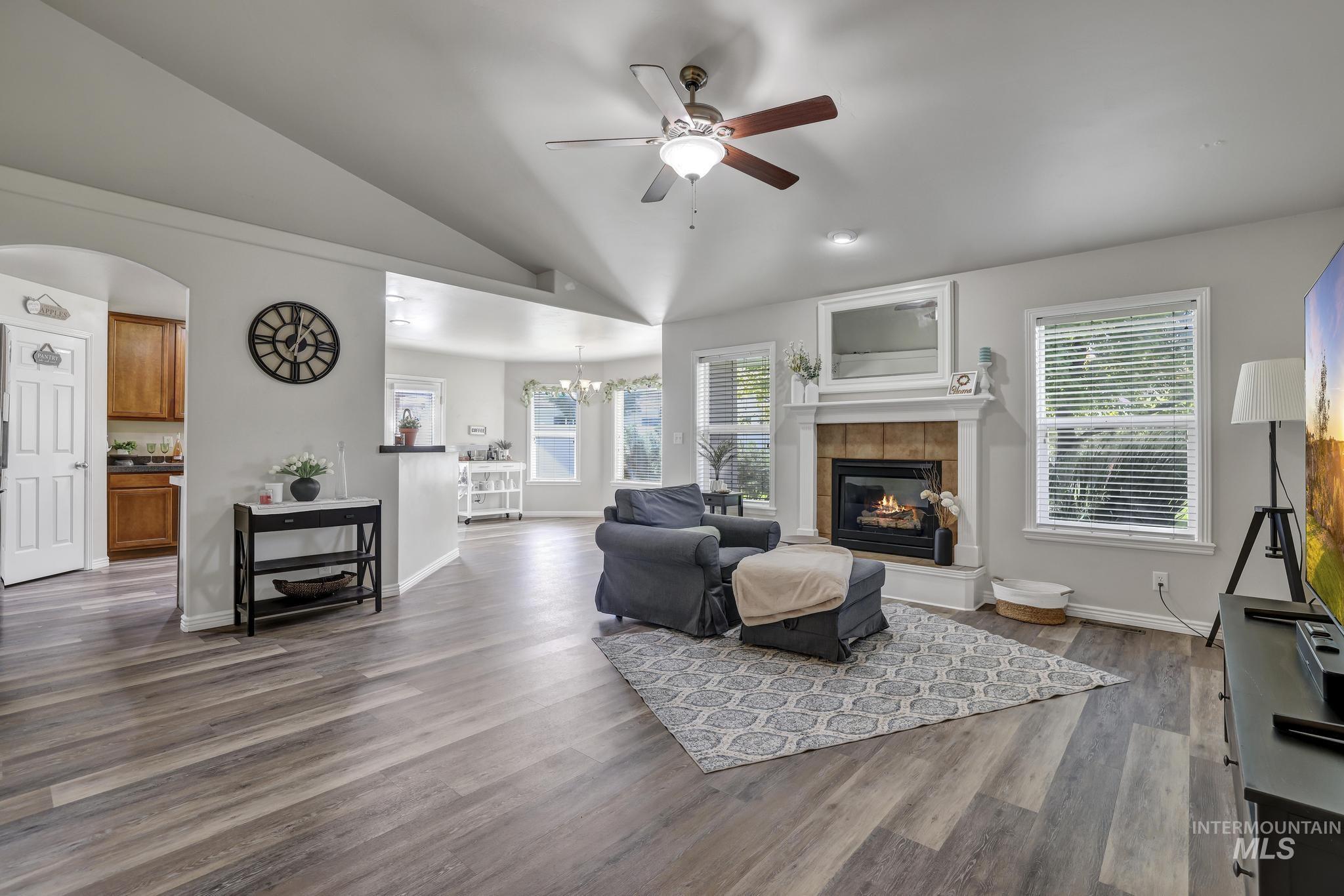 Living room featuring vaulted ceiling, a ceiling fan, dark wood finished floors, a fireplace, and healthy amount of natural light