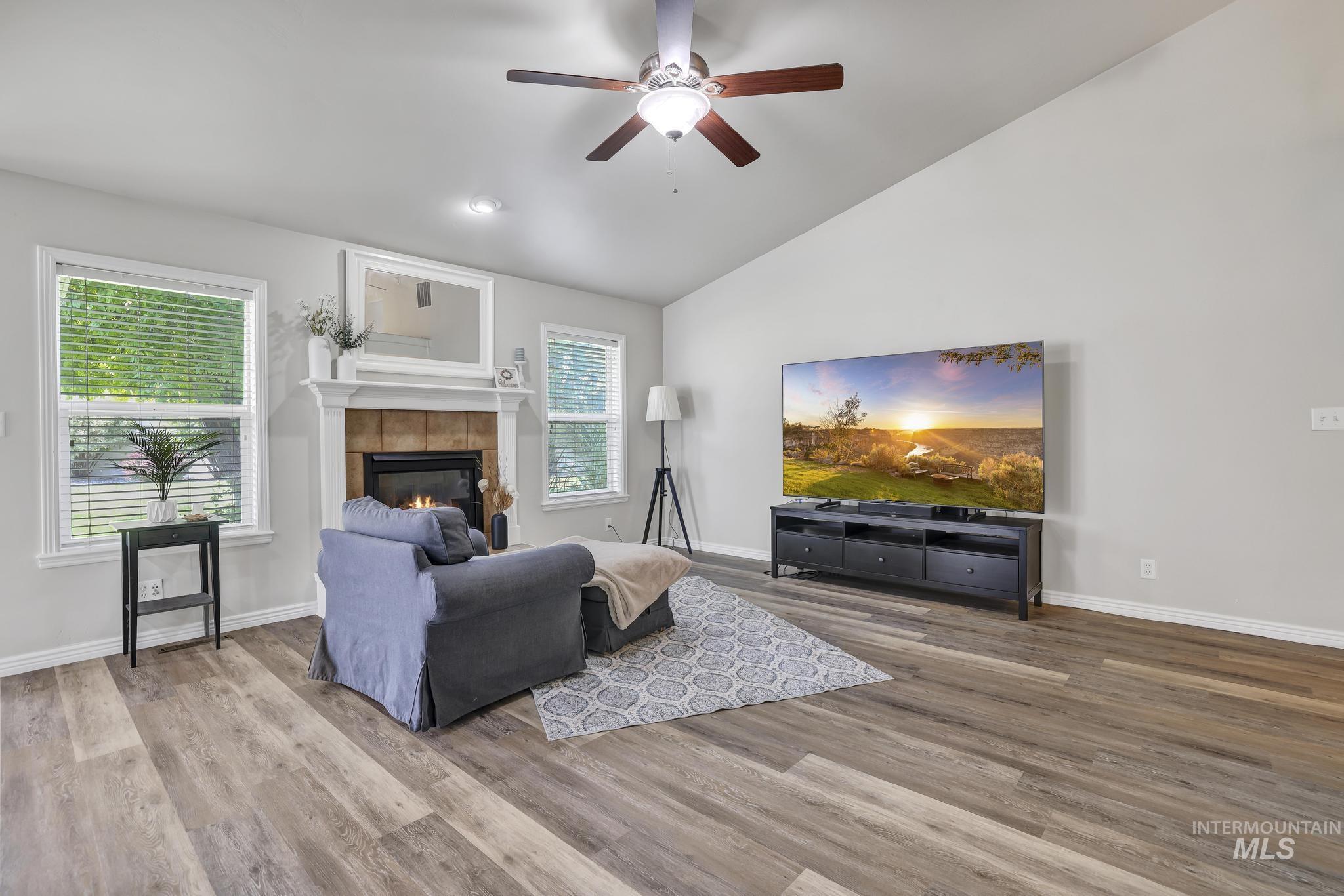 Living room with a tile fireplace, ceiling fan, wood finished floors, and high vaulted ceiling