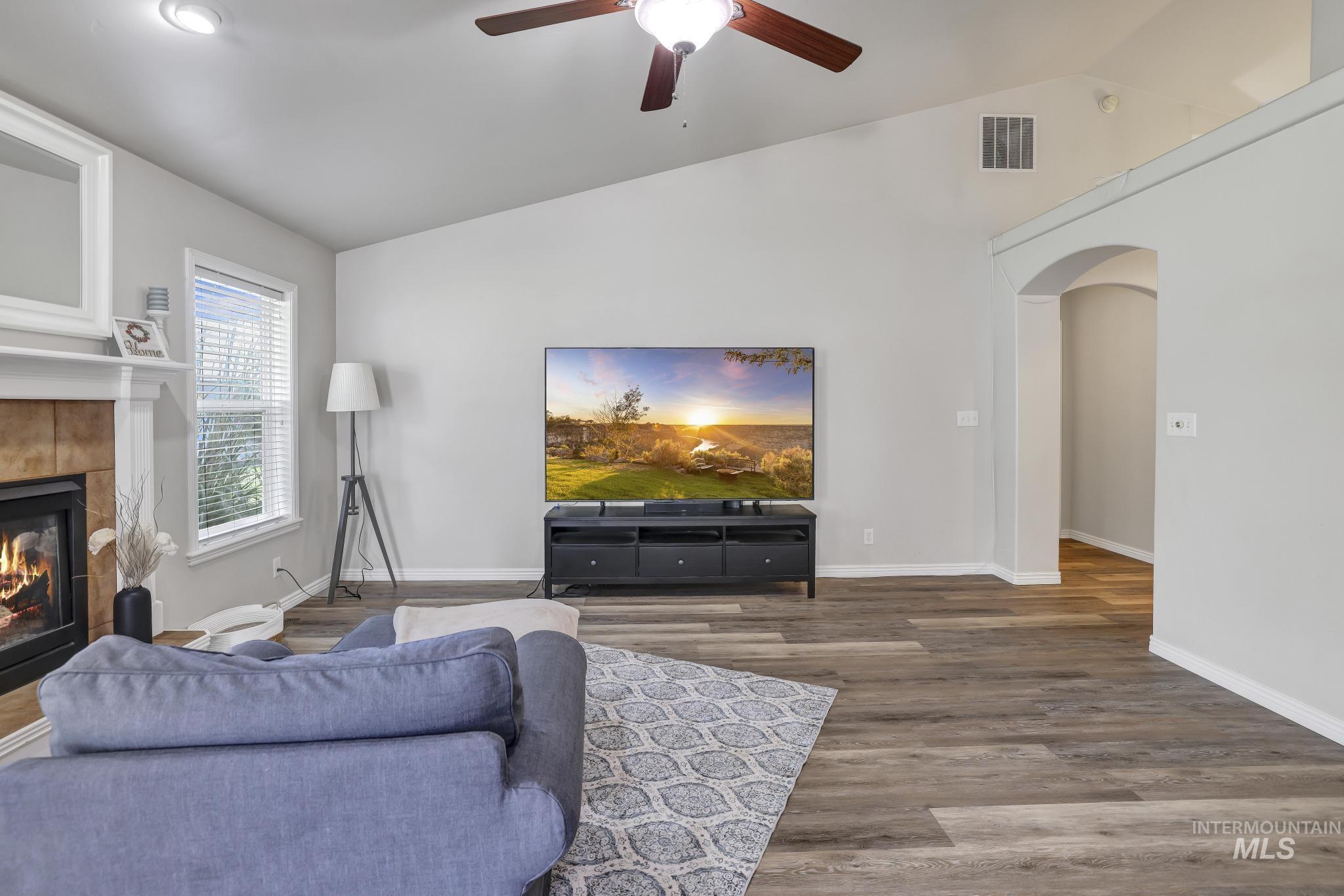 Living area with vaulted ceiling, arched walkways, wood finished floors, a ceiling fan, and a tile fireplace