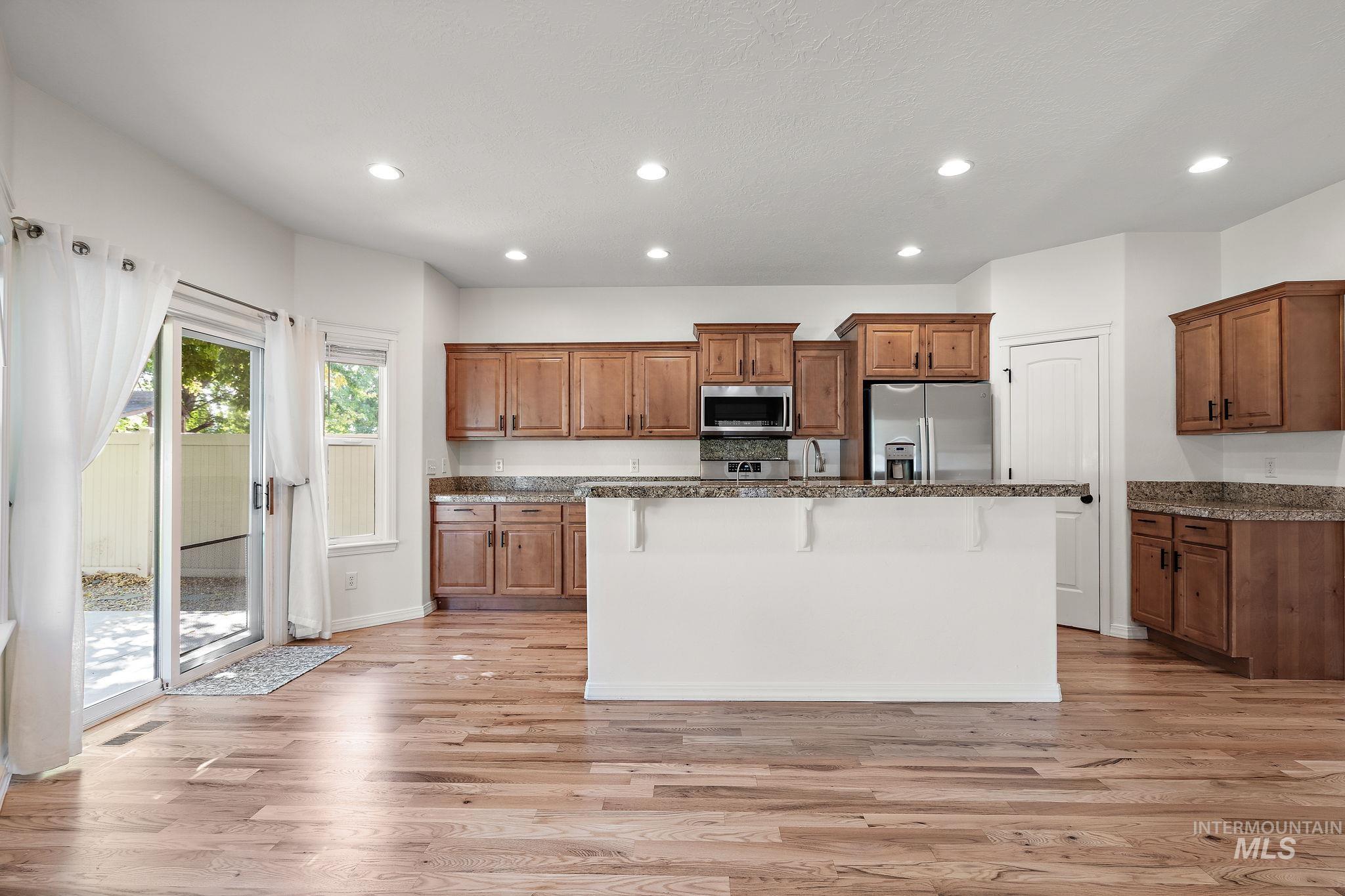 Kitchen featuring brown cabinets, a breakfast bar, recessed lighting, dark stone countertops, and light wood-style flooring