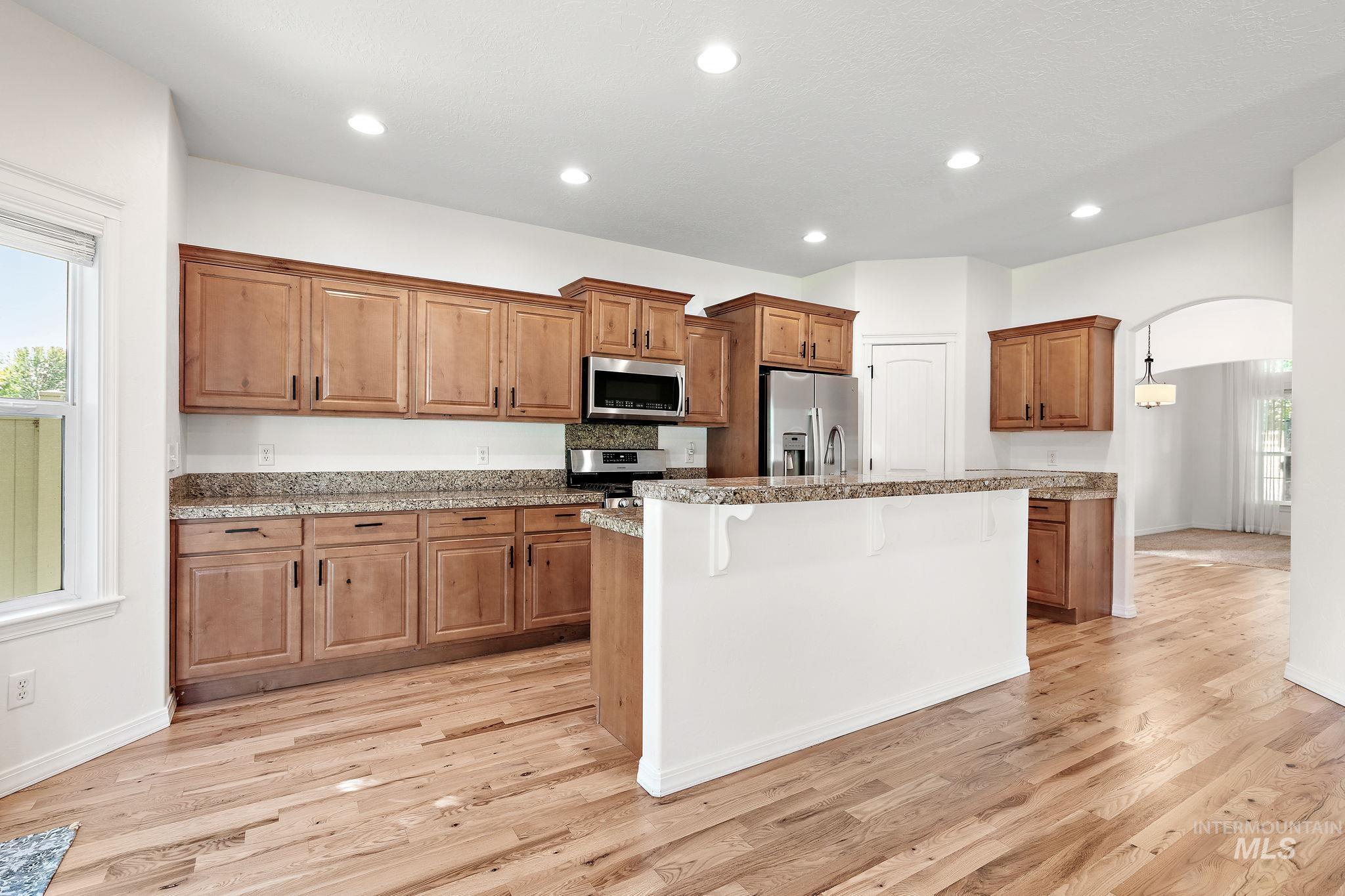 Kitchen with a kitchen breakfast bar, arched walkways, brown cabinets, recessed lighting, and appliances with stainless steel finishes