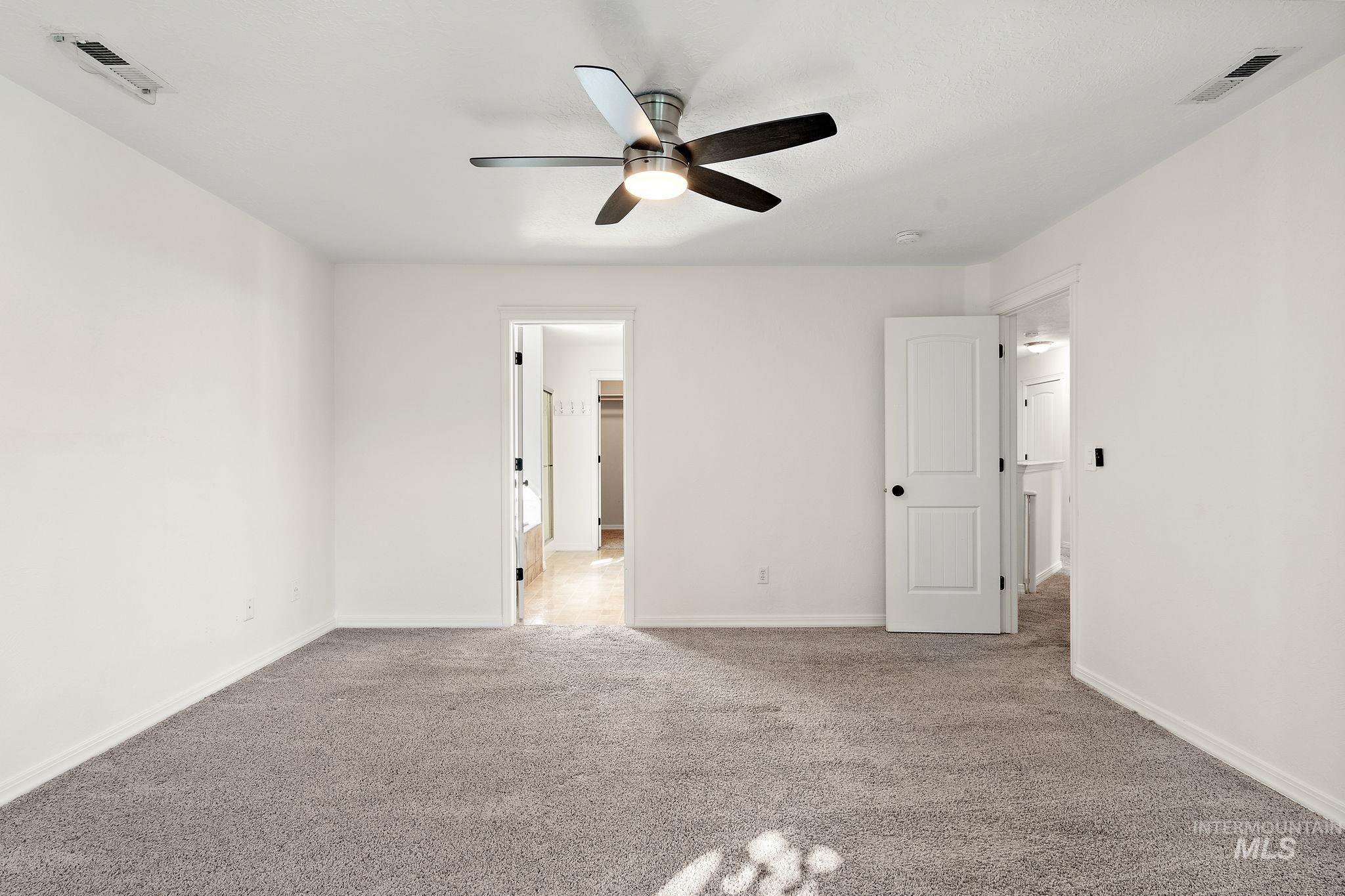 Unfurnished bedroom with light colored carpet, ceiling fan, and ensuite bath