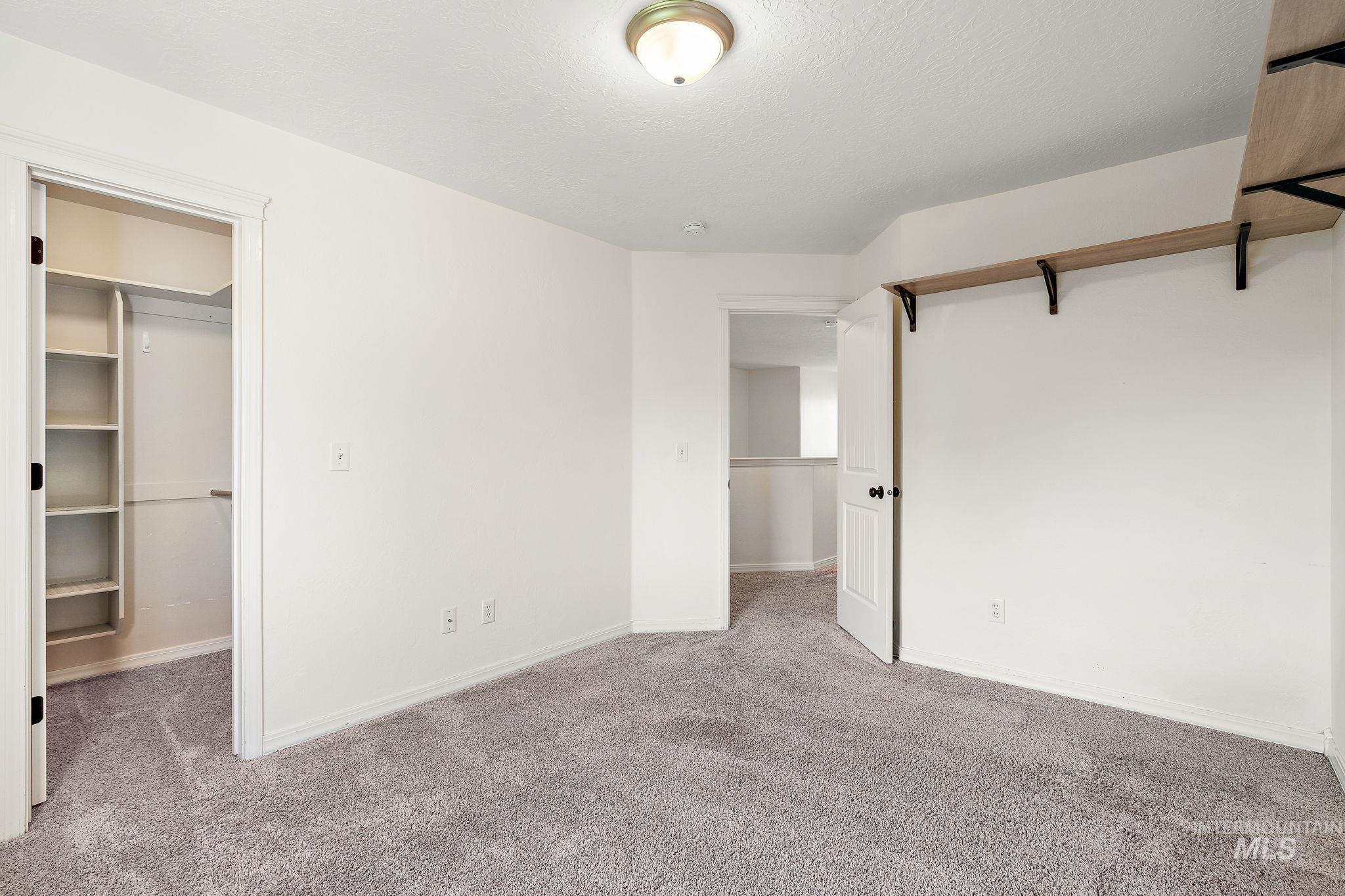 Unfurnished bedroom with carpet floors, a walk in closet, and a textured ceiling