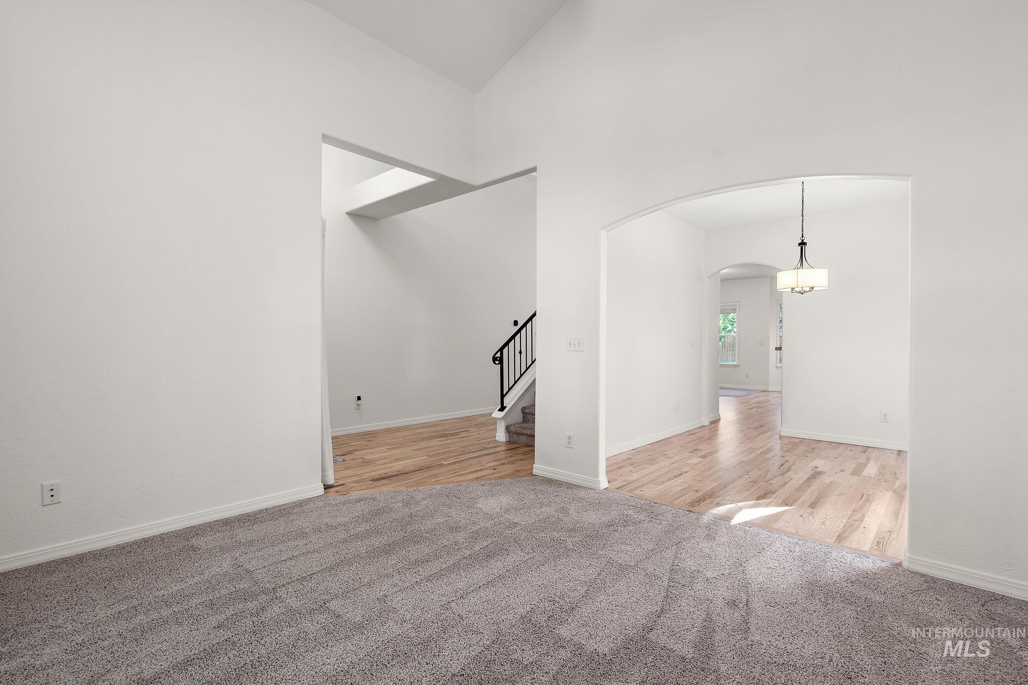 Unfurnished room featuring light colored carpet, arched walkways, stairway, and high vaulted ceiling