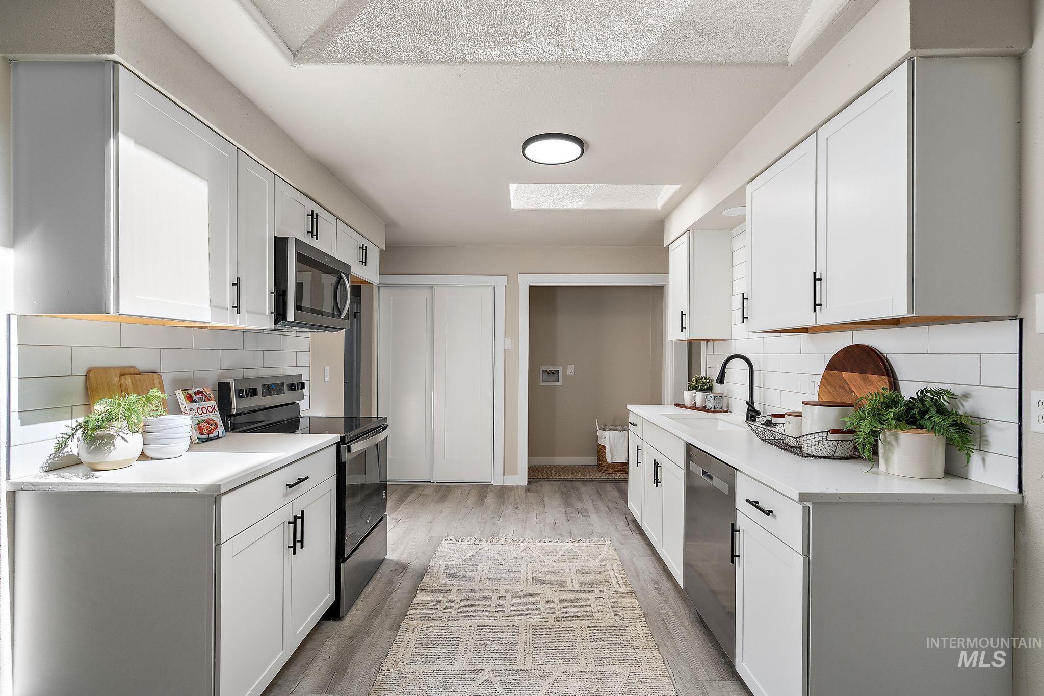Kitchen featuring decorative backsplash, appliances with stainless steel finishes, white cabinetry, and light wood-style flooring