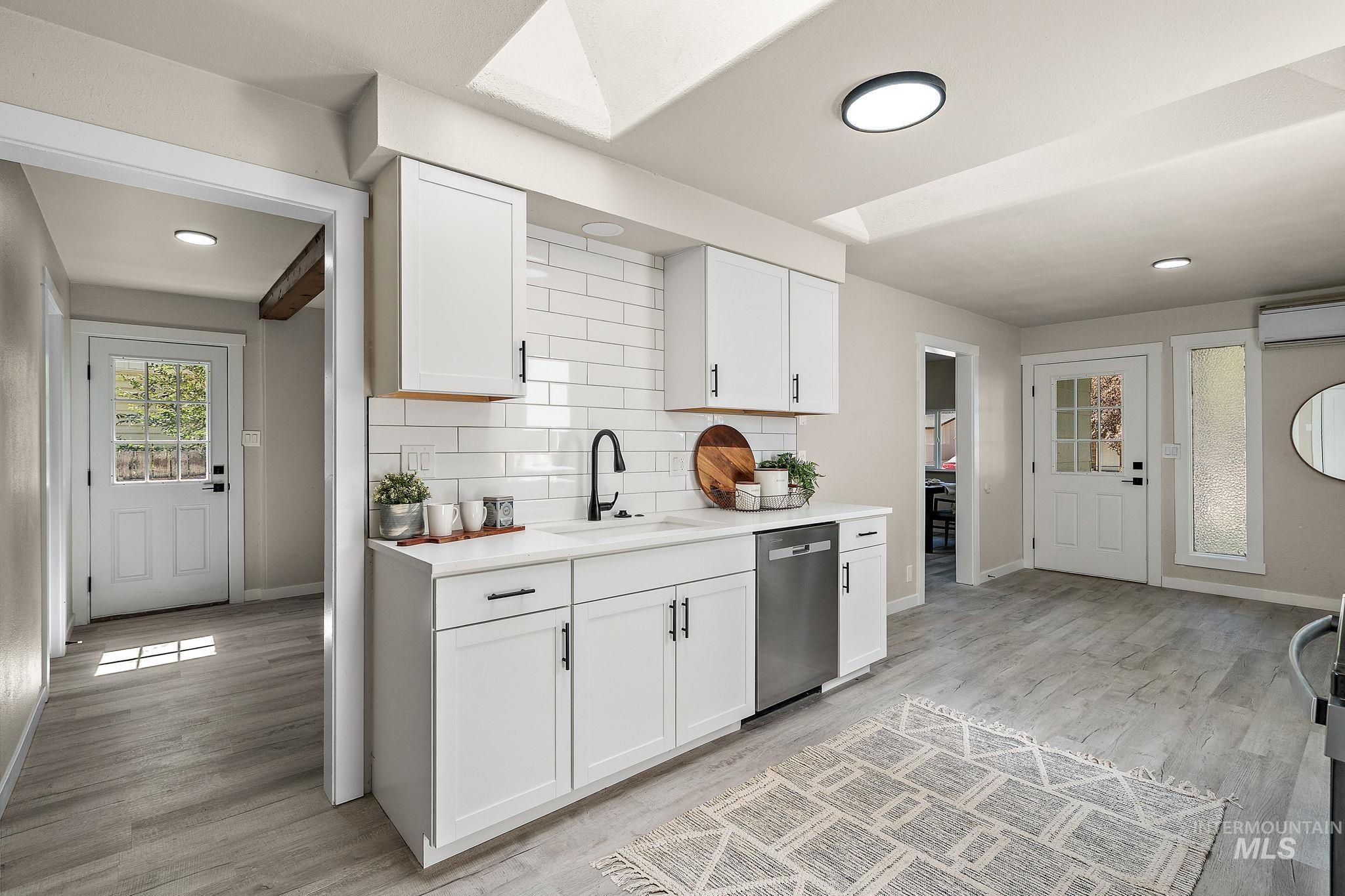 Kitchen with white cabinetry, light wood-style floors, decorative backsplash, stainless steel dishwasher, and recessed lighting