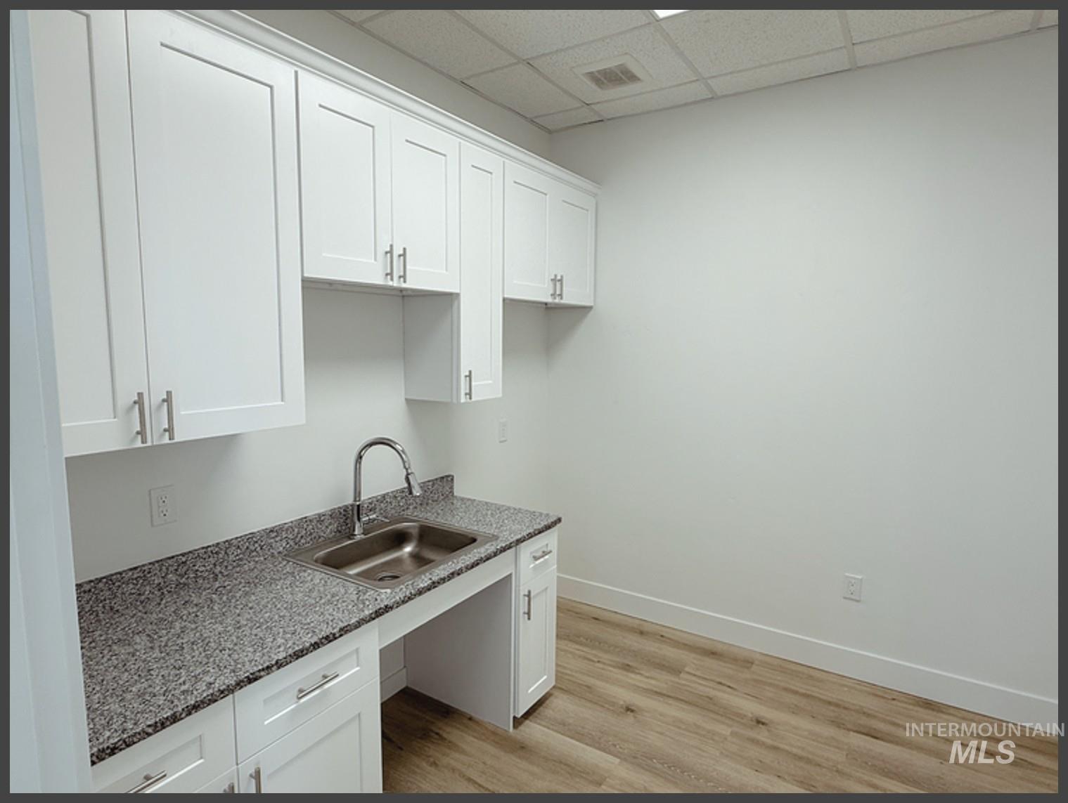 Kitchen with white cabinetry, light wood-type flooring, a drop ceiling, and dark stone counters