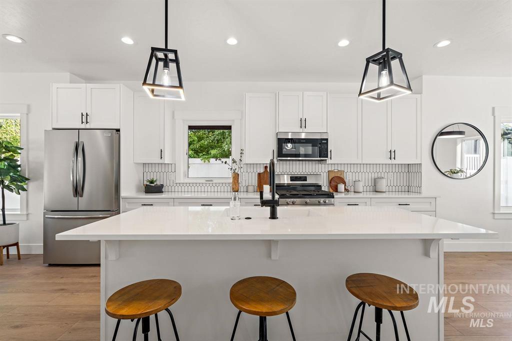 Kitchen featuring appliances with stainless steel finishes, tasteful backsplash, white cabinets, a breakfast bar, and recessed lighting