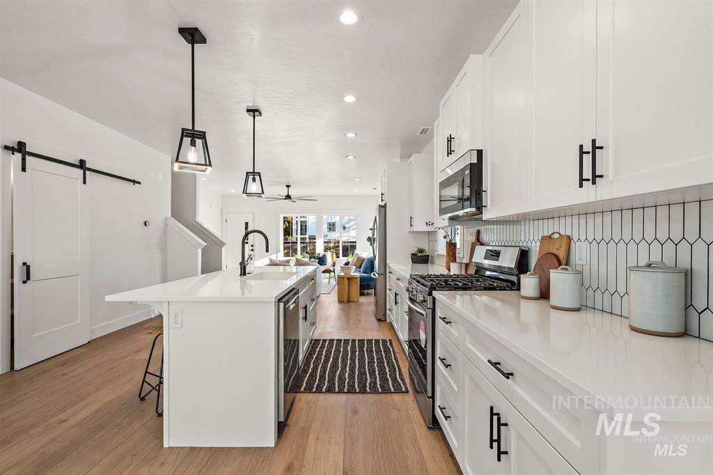 Kitchen with a barn door, appliances with stainless steel finishes, a kitchen island with sink, a kitchen bar, and white cabinetry