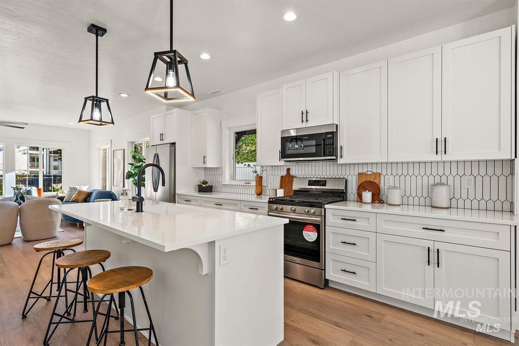 Kitchen with open floor plan, appliances with stainless steel finishes, a kitchen breakfast bar, a center island with sink, and pendant lighting