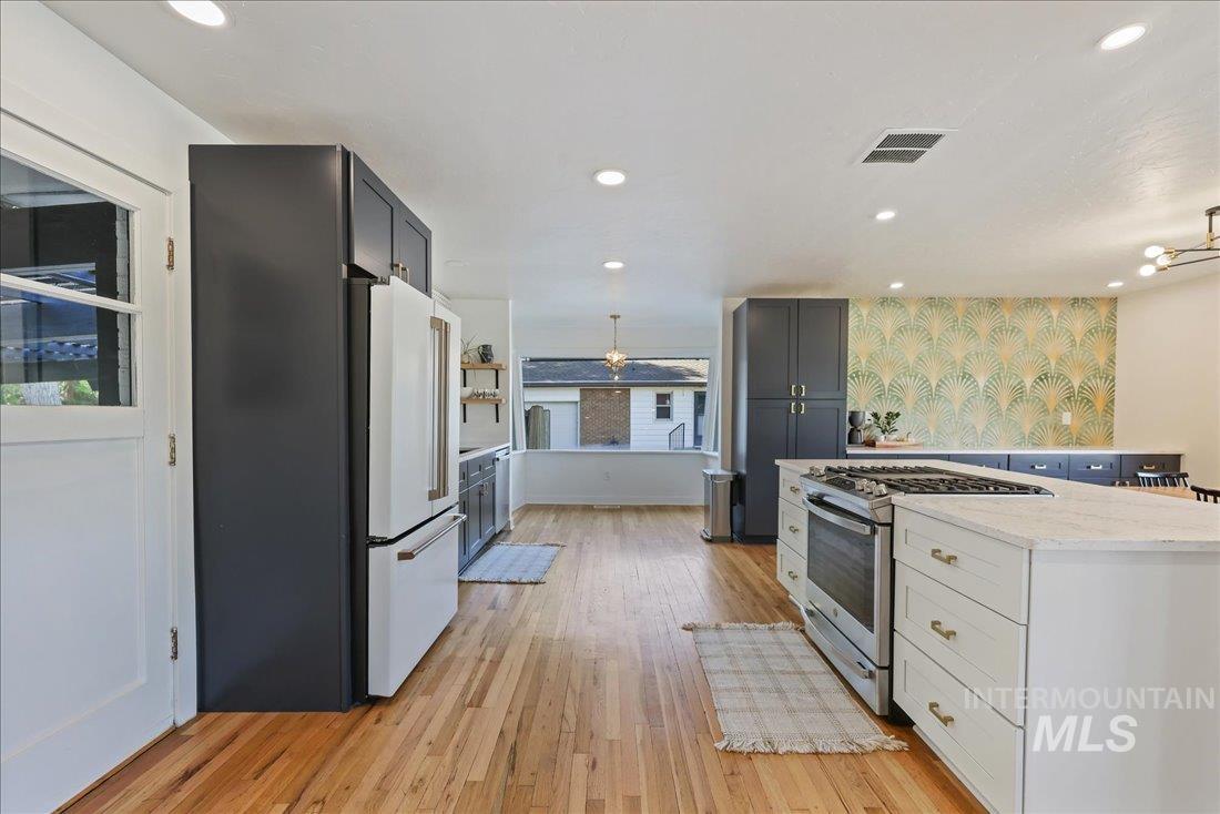 Kitchen with stainless steel gas stove, high end fridge, light wood-style floors, light stone countertops, and recessed lighting
