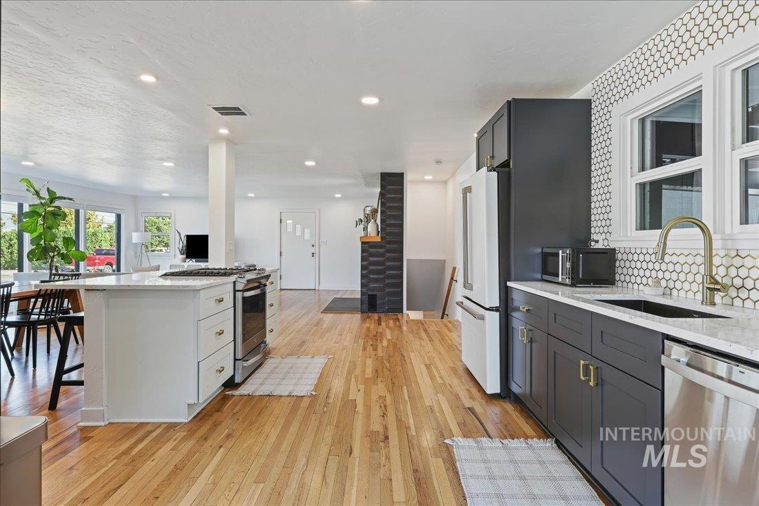 Kitchen with light stone countertops, appliances with stainless steel finishes, light wood-style floors, recessed lighting, and decorative backsplash