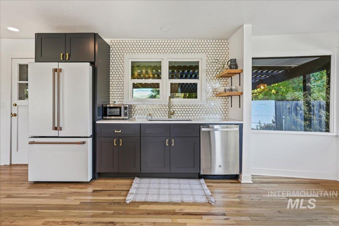 Kitchen with appliances with stainless steel finishes, healthy amount of natural light, open shelves, and light stone counters