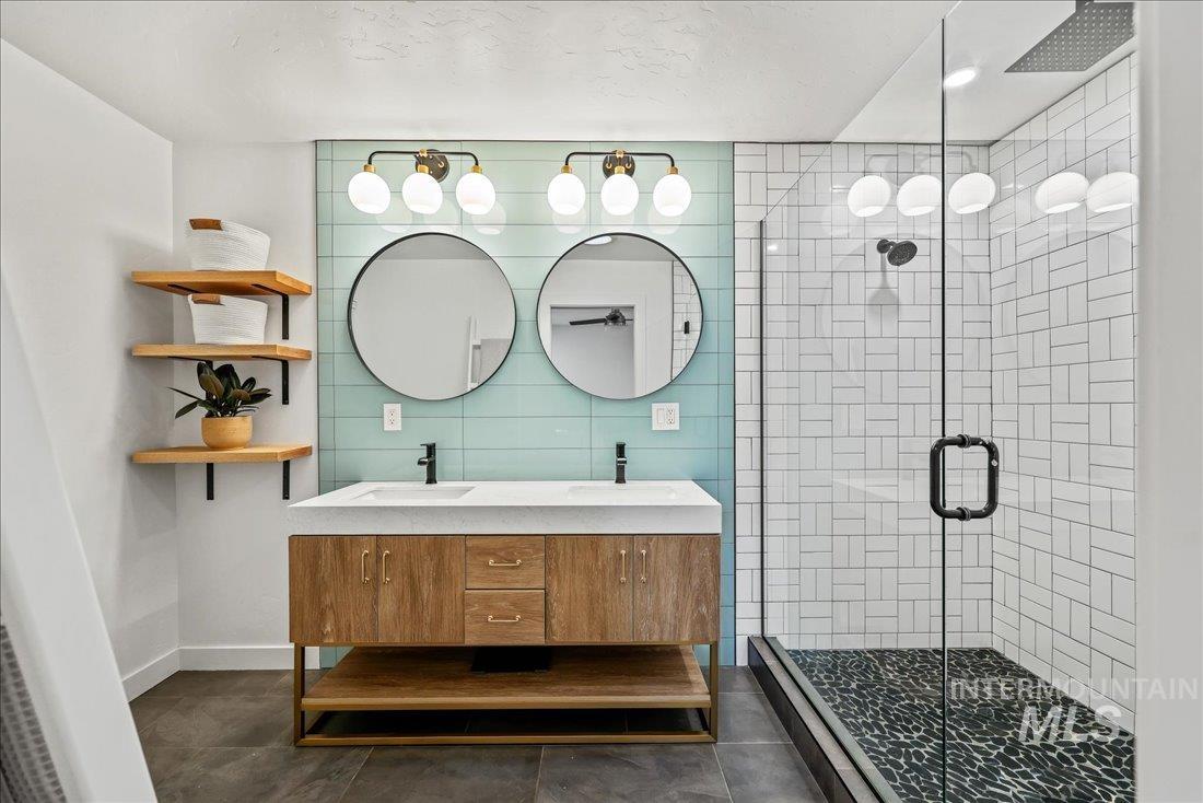Bathroom featuring double vanity, a stall shower, dark tile patterned floors, and tile walls
