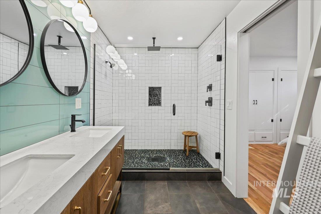 Bathroom with a shower stall, double vanity, dark tile patterned floors, and recessed lighting