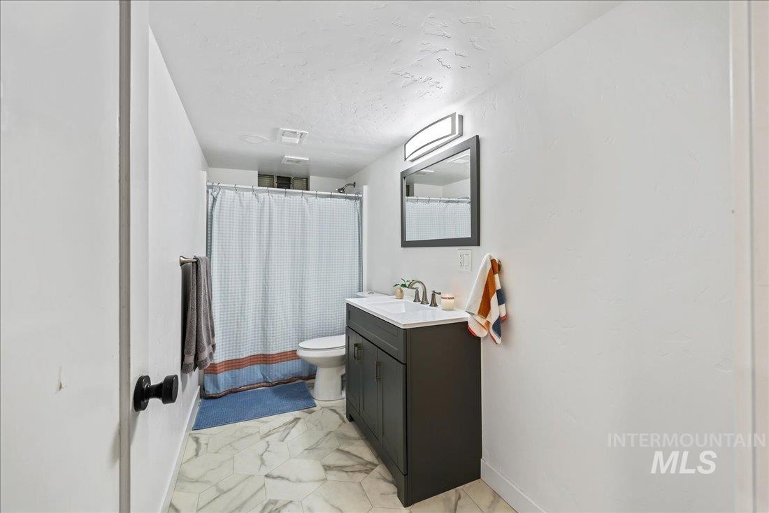 Full bath featuring vanity, a textured ceiling, shower / tub combo, and light marble finish flooring
