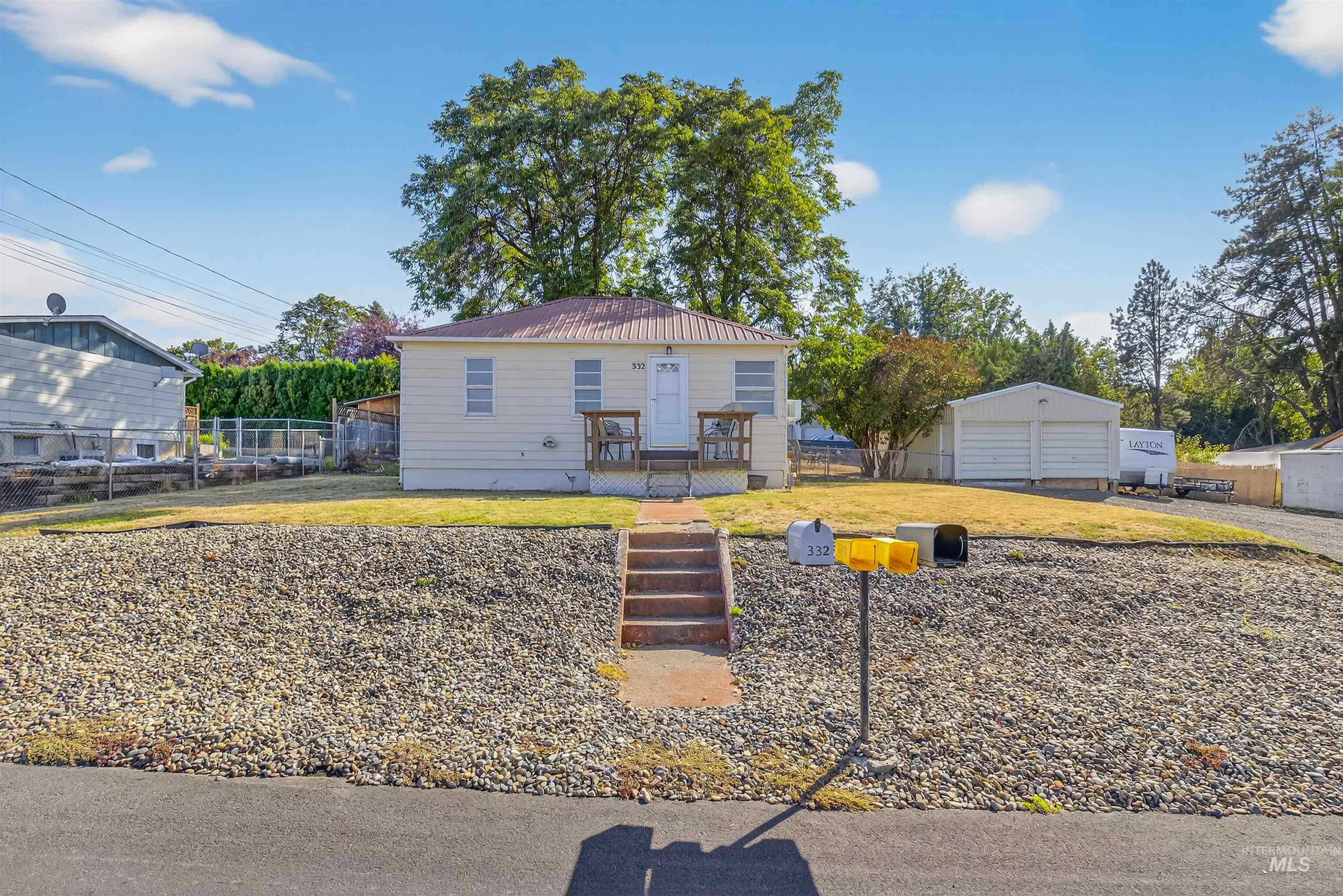 Bungalow-style house with a metal roof, a detached garage, a wooden deck, and an outbuilding