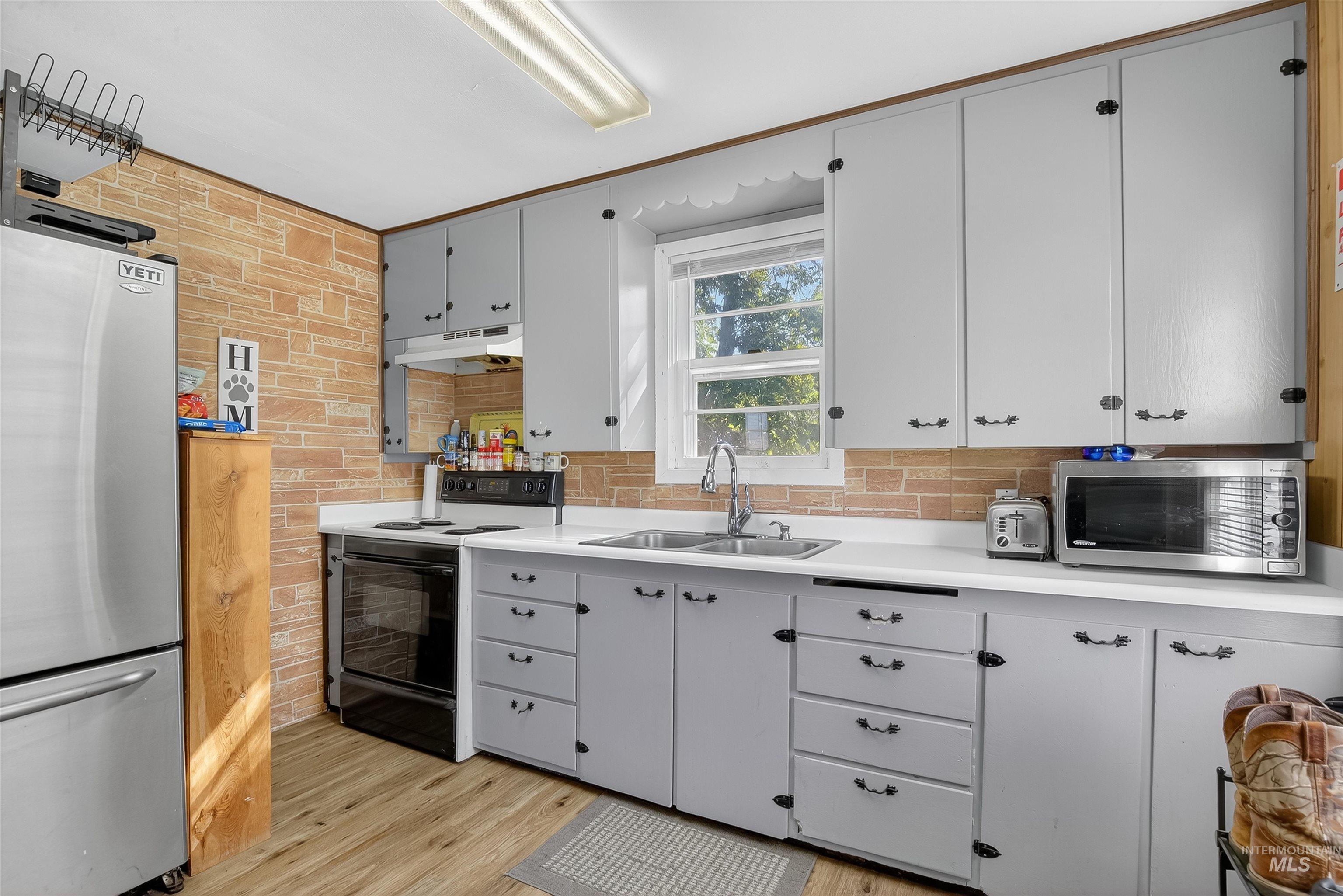 Kitchen with stainless steel appliances, light countertops, light wood-style floors, under cabinet range hood, and gray cabinetry