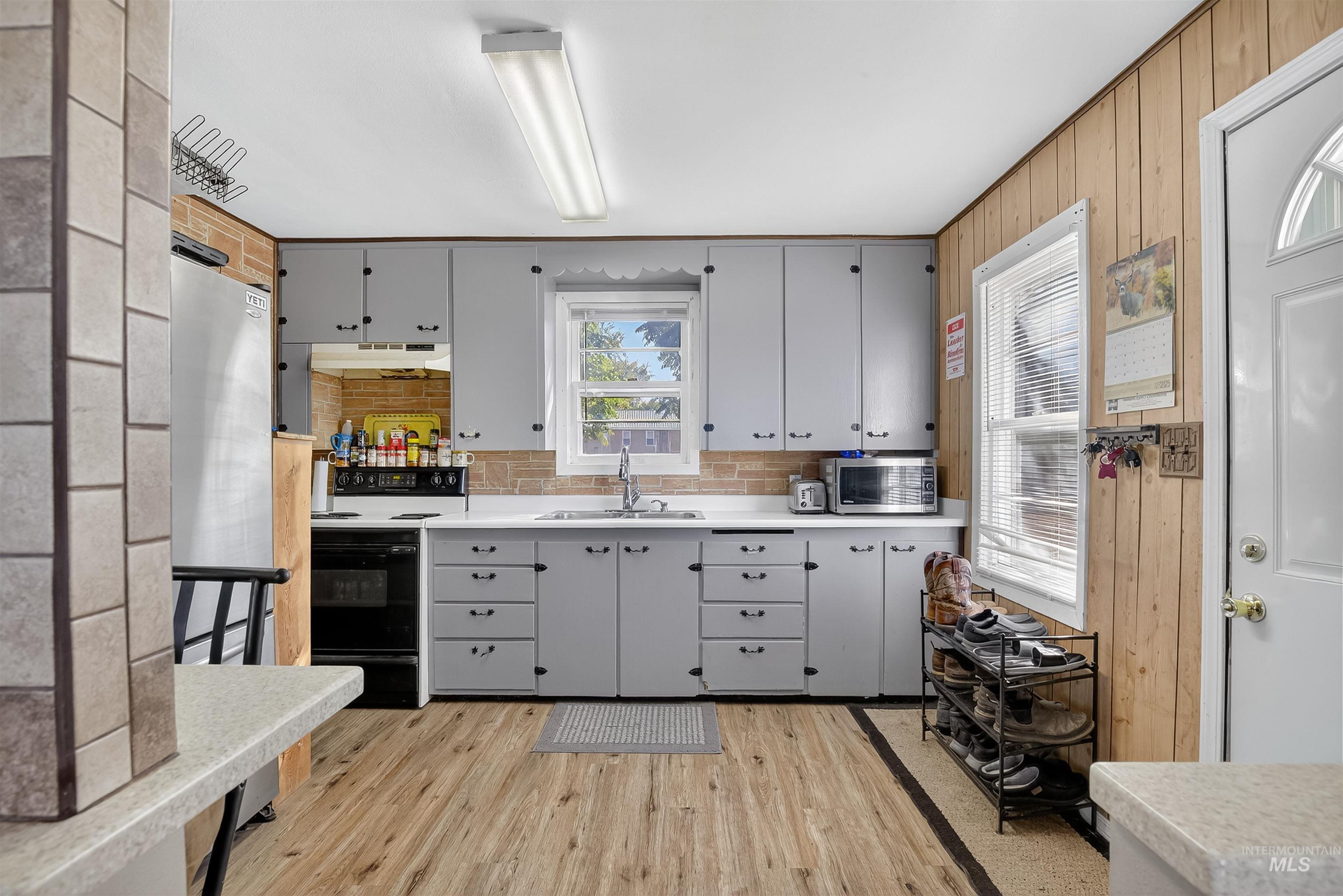 Kitchen with gray cabinetry, light countertops, appliances with stainless steel finishes, light wood-style flooring, and tasteful backsplash