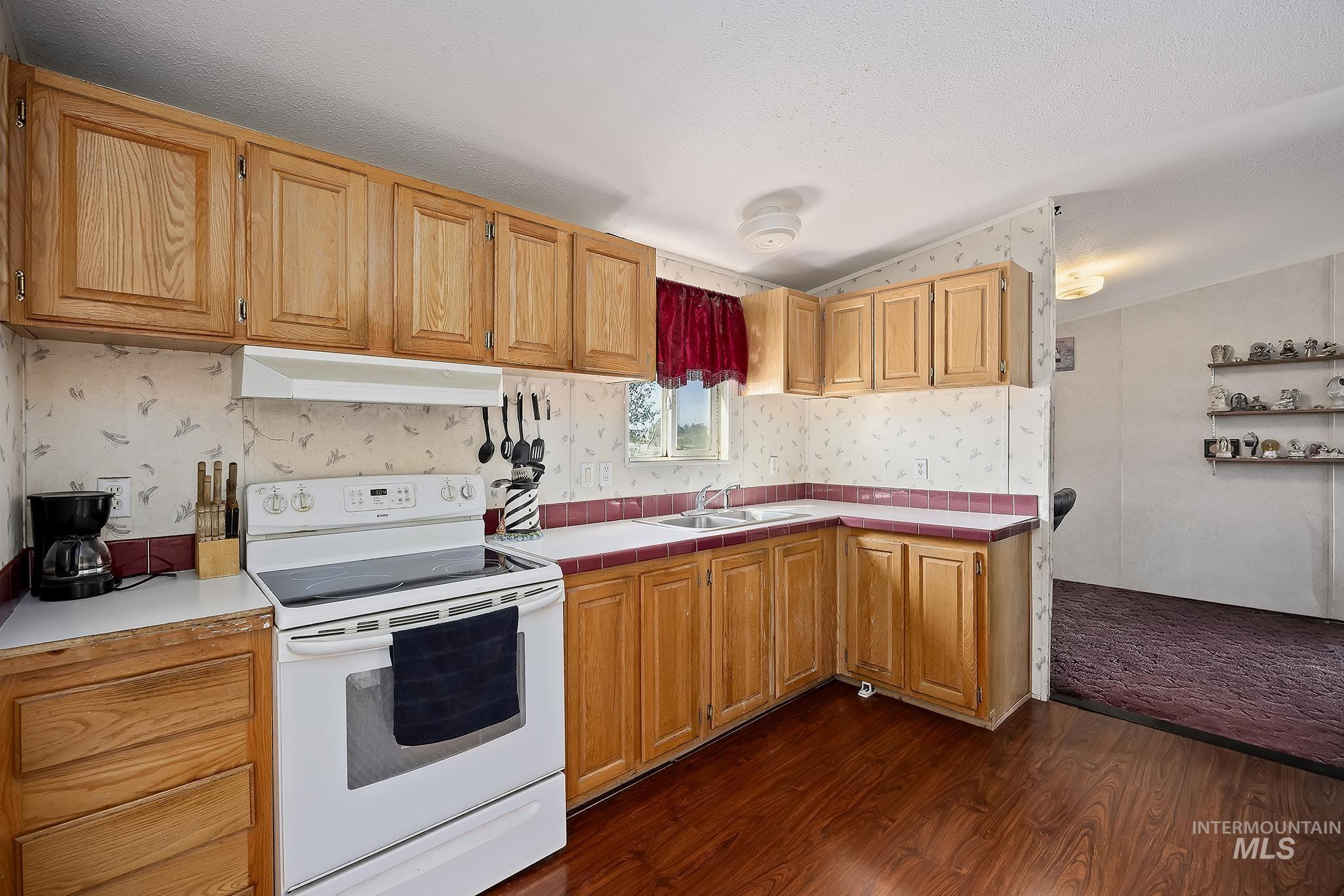 Kitchen featuring white electric range oven, dark wood finished floors, vaulted ceiling, wallpapered walls, and under cabinet range hood
