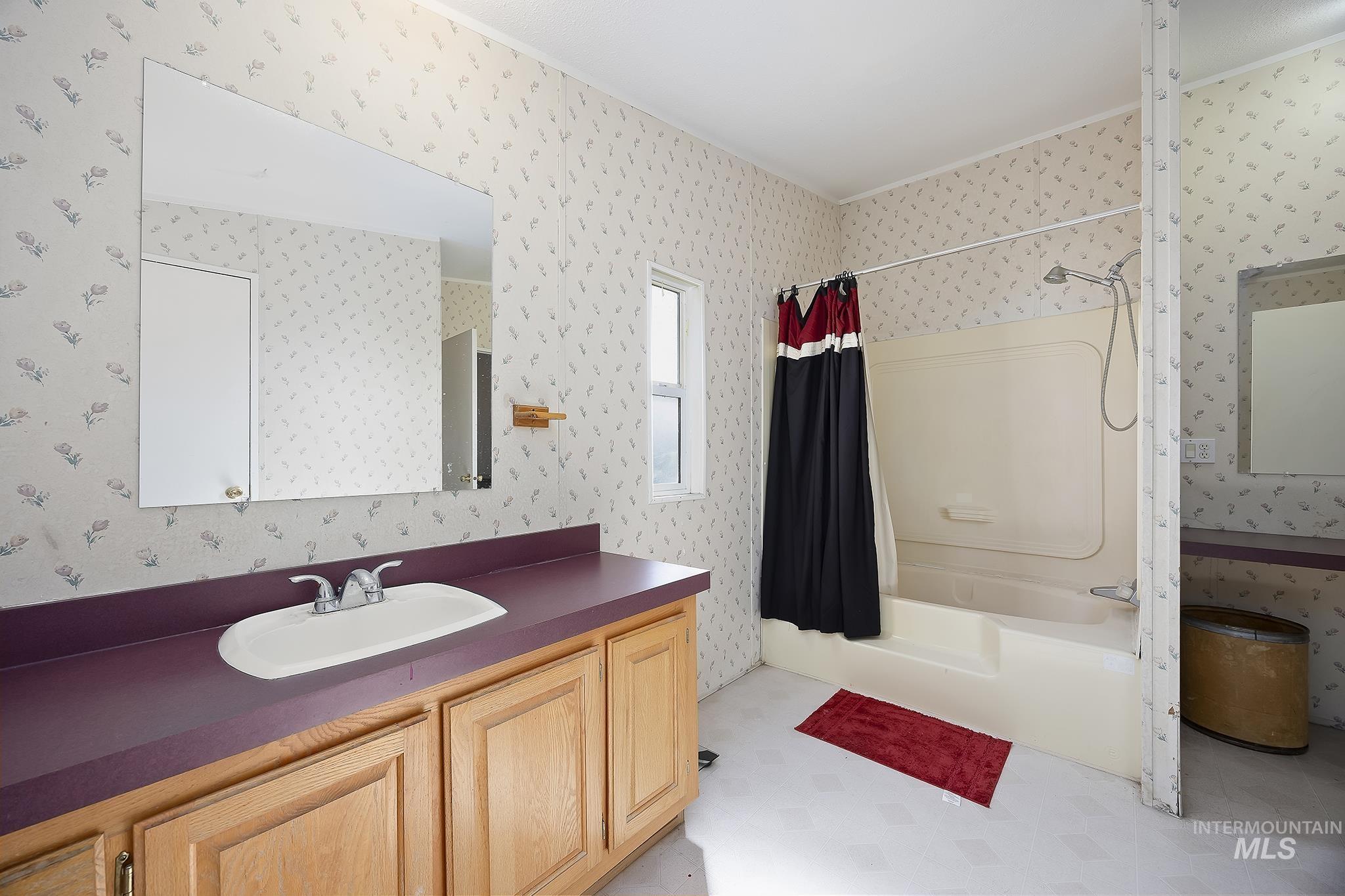 Bathroom featuring shower / bathtub combination with curtain, vanity, and wallpapered walls