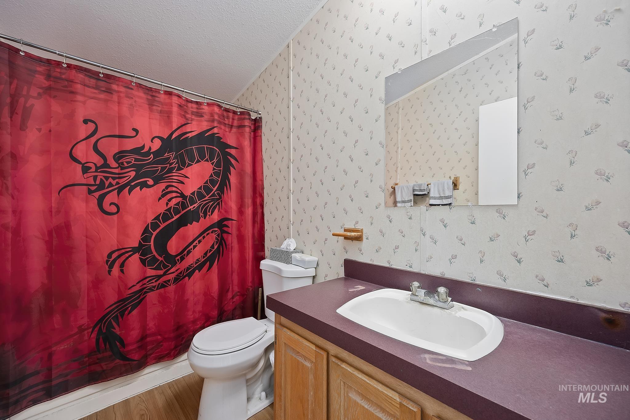 Full bath featuring vanity, a textured ceiling, a shower with curtain, wallpapered walls, and wood finished floors