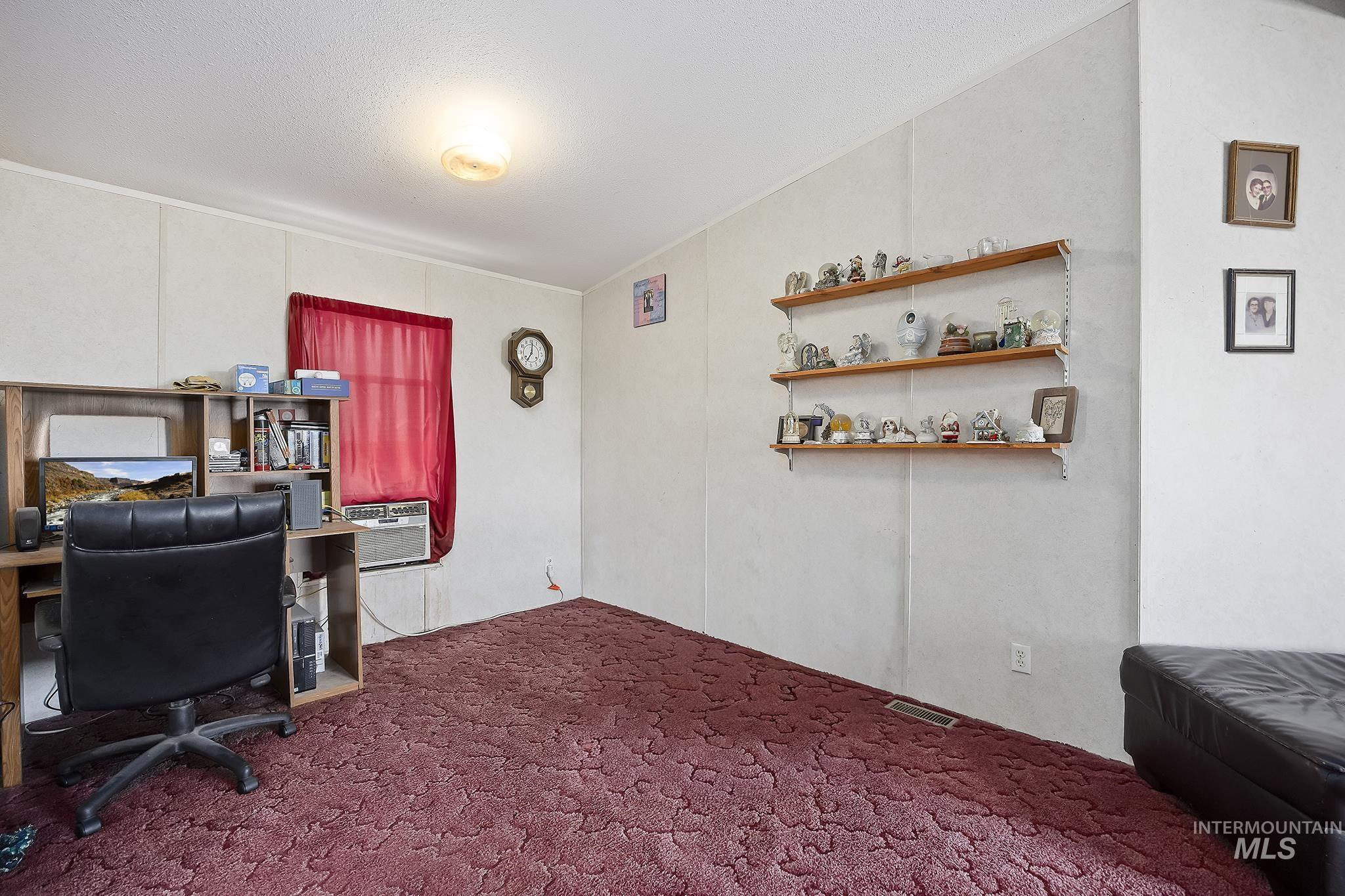 Home office with dark colored carpet, a decorative wall, and a textured ceiling