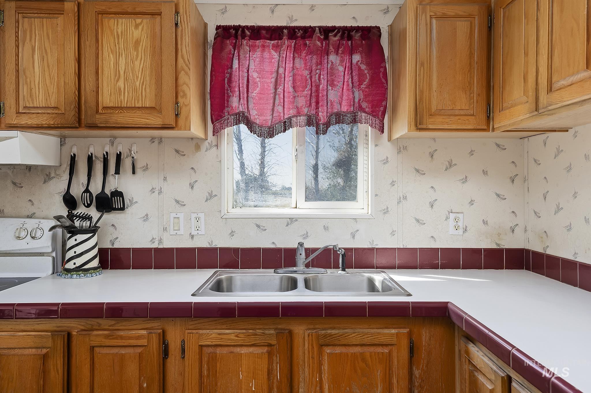 Kitchen with wallpapered walls, white stove, brown cabinets, light countertops, and extractor fan